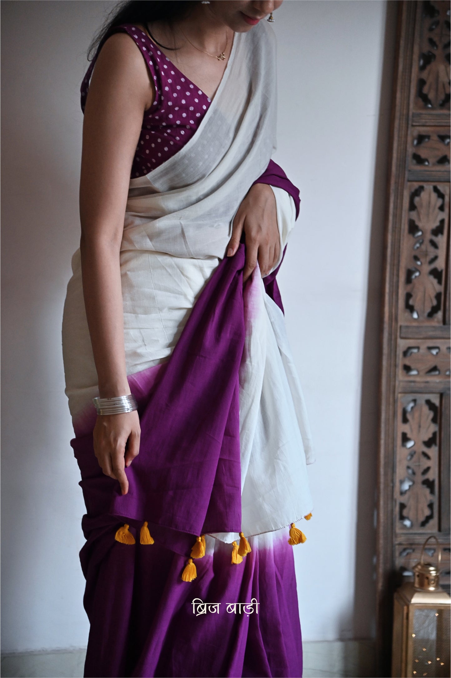 Purple and off-white ombré soft cotton saree by Brij Bari, crafted for effortless elegance and all-day comfort. The subtle blend of tones adds fluidity and grace to the drape, making it perfect for both everyday wear and special occasions. The pallu is adorned with handcrafted yellow thread tassels, lending a warm, artisanal touch. It comes with a free hand block printed blouse piece that complements the saree’s minimal yet striking aesthetic. Available in 8 beautiful colour options
