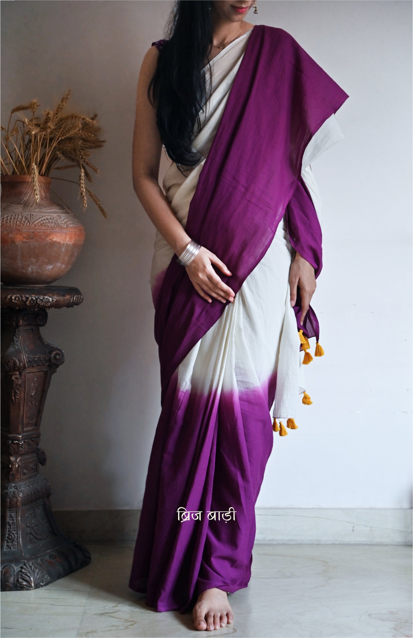 Purple and off-white ombré soft cotton saree by Brij Bari, crafted for effortless elegance and all-day comfort. The subtle blend of tones adds fluidity and grace to the drape, making it perfect for both everyday wear and special occasions. The pallu is adorned with handcrafted yellow thread tassels, lending a warm, artisanal touch. It comes with a free hand block printed blouse piece that complements the saree’s minimal yet striking aesthetic. Available in 8 beautiful colour options
