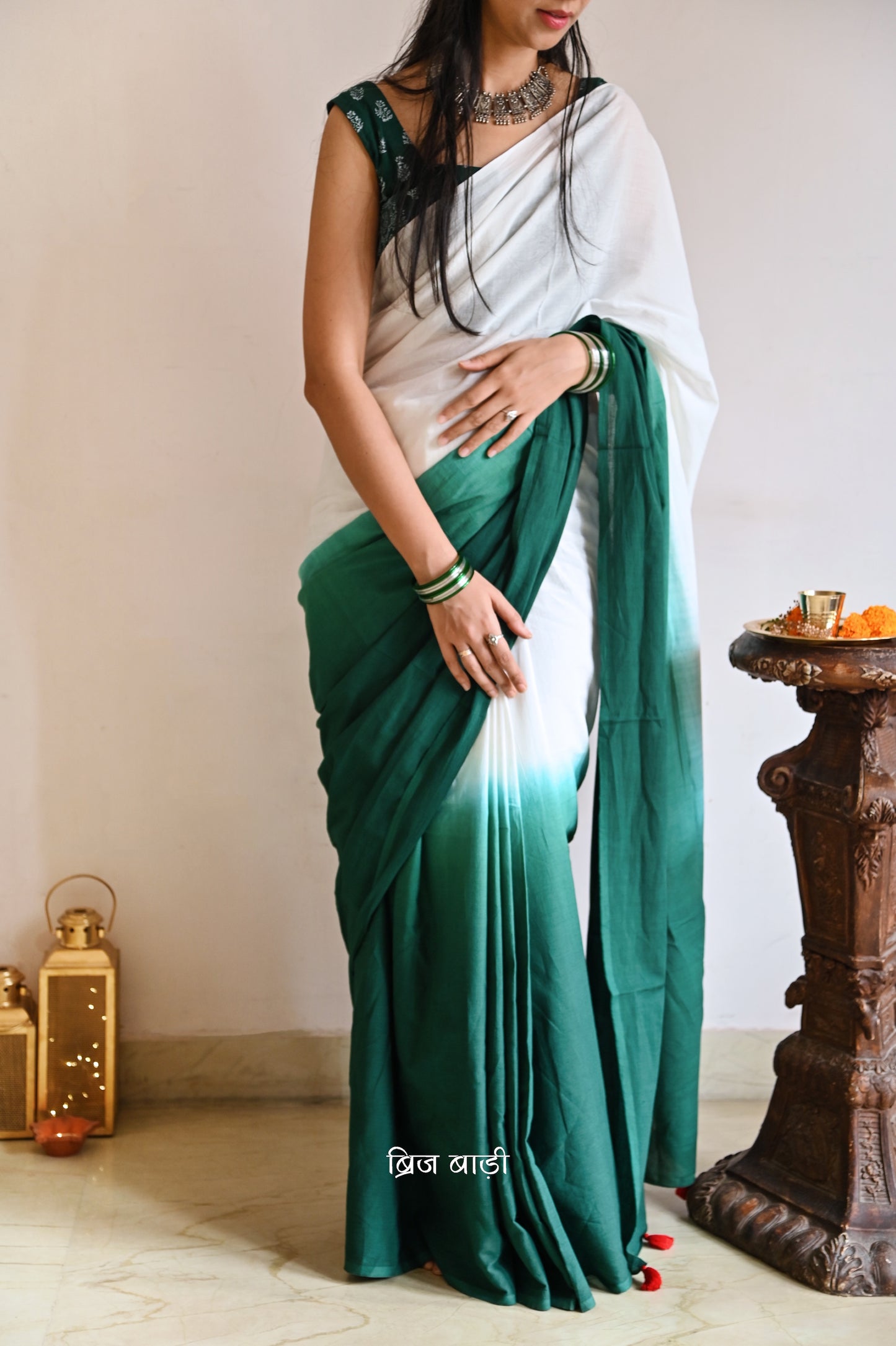 Dark Green and off-white ombré soft cotton saree by Brij Bari, crafted for effortless elegance and all-day comfort. The subtle blend of tones adds fluidity and grace to the drape, making it perfect for both everyday wear and special occasions. The pallu is adorned with handcrafted red thread tassels, lending a warm, artisanal touch. It comes with a free hand block printed blouse piece that complements the saree’s minimal yet striking aesthetic. Available in 8 beautiful colour options