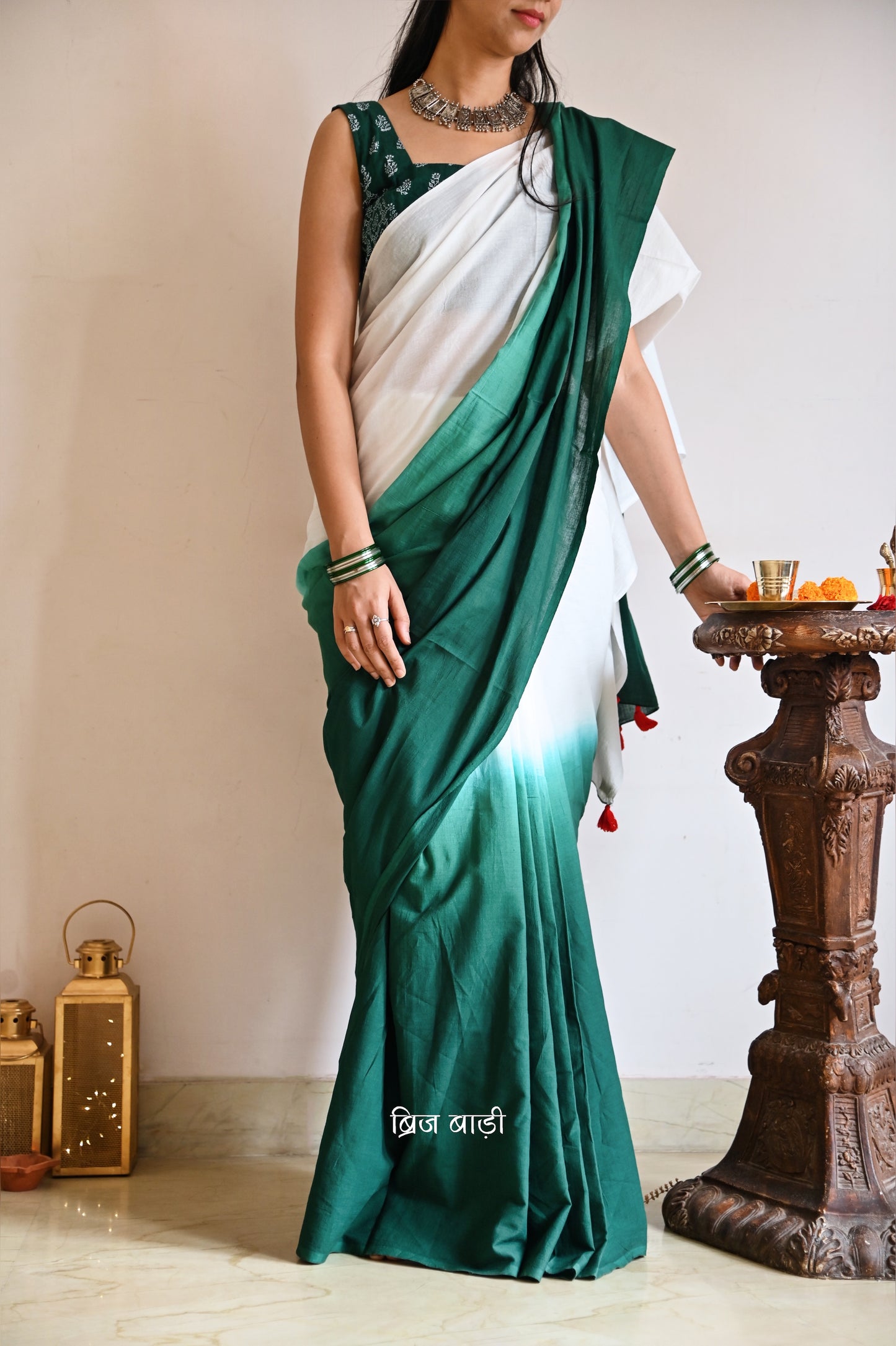 Dark Green and off-white ombré soft cotton saree by Brij Bari, crafted for effortless elegance and all-day comfort. The subtle blend of tones adds fluidity and grace to the drape, making it perfect for both everyday wear and special occasions. The pallu is adorned with handcrafted red thread tassels, lending a warm, artisanal touch. It comes with a free hand block printed blouse piece that complements the saree’s minimal yet striking aesthetic. Available in 8 beautiful colour options