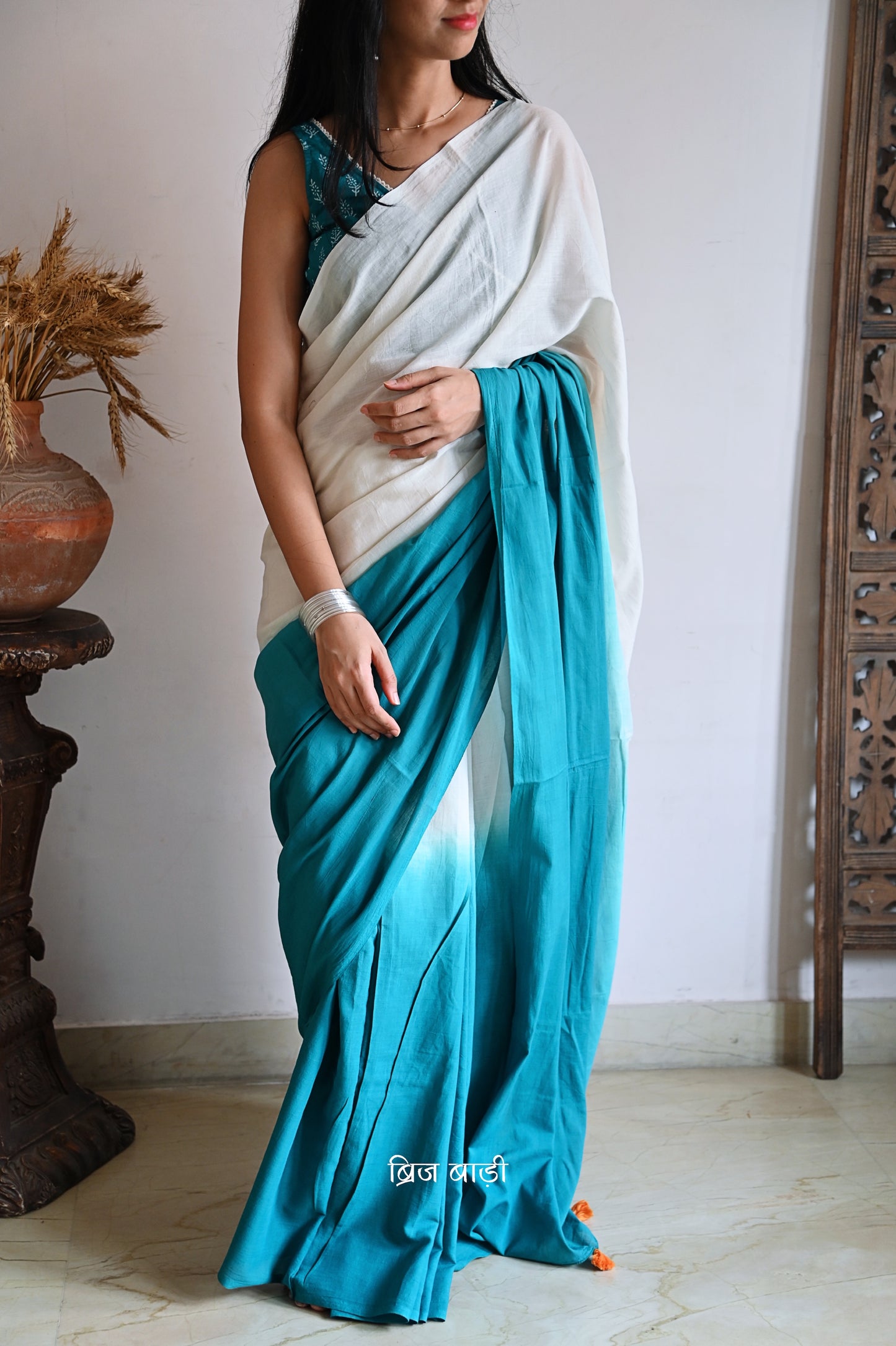 Teal Blue and off-white ombré soft cotton saree by Brij Bari, crafted for effortless elegance and all-day comfort. The subtle blend of tones adds fluidity and grace to the drape, making it perfect for both everyday wear and special occasions. The pallu is adorned with handcrafted orange thread tassels, lending a warm, artisanal touch. It comes with a free hand block printed blouse piece that complements the saree’s minimal yet striking aesthetic. Available in 8 beautiful colour options