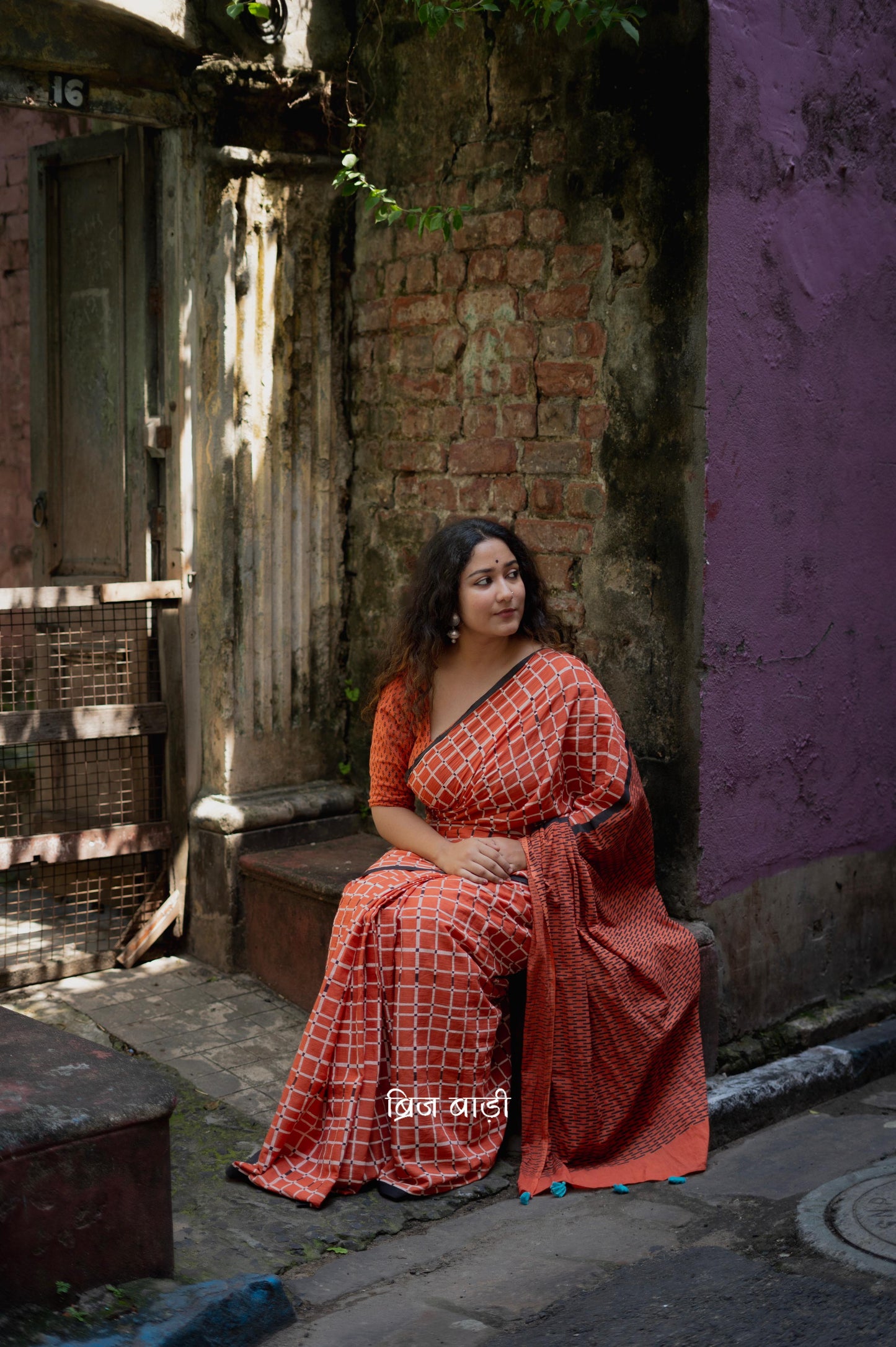 Earthy rust cotton saree by Brij Bari, hand block printed with black and white check pattern. Designed in soft, lightweight cotton with handmade light blue thread tassels on the pallu. Includes a free hand block printed cotton blouse piece. Perfect for adding a handcrafted, artisanal touch to your daily wear with breathable comfort and effortless style. Free shipping pan India.
