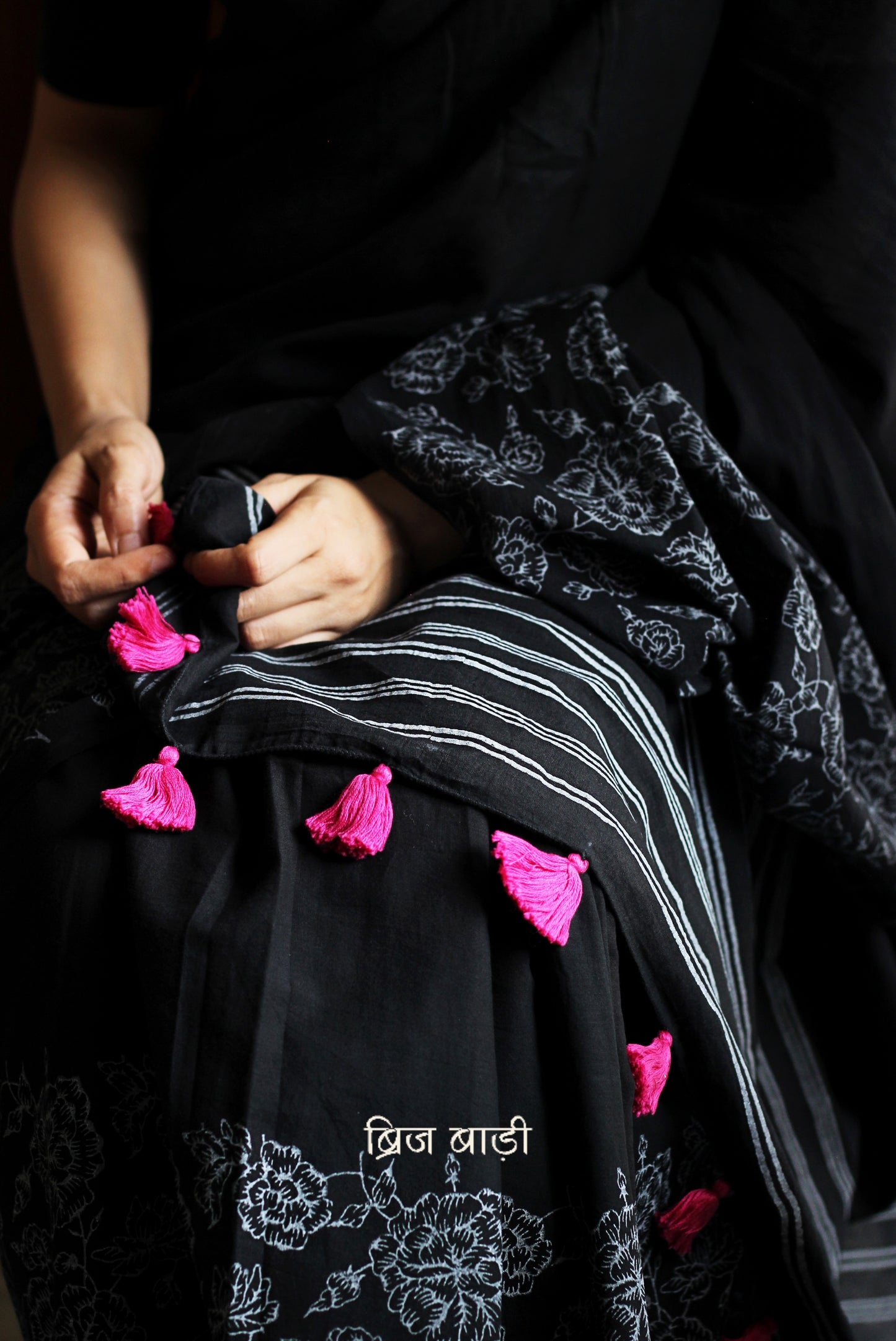 Black soft and light-weight cotton saree by Brij Bari, hand block printed with a graceful rose pattern on the skirt and contrasting bold stripes on the pallu. This versatile, breathable saree is designed for everyday ease — lightweight, elegant, and comfortable, perfect for casual outings & office wear. Finished with charming pink handmade thread tassels on the pallu. Comes with a free hand block printed blouse piece designed to compliment the sare’s floral and striped patterns. Free shipping pan India.
