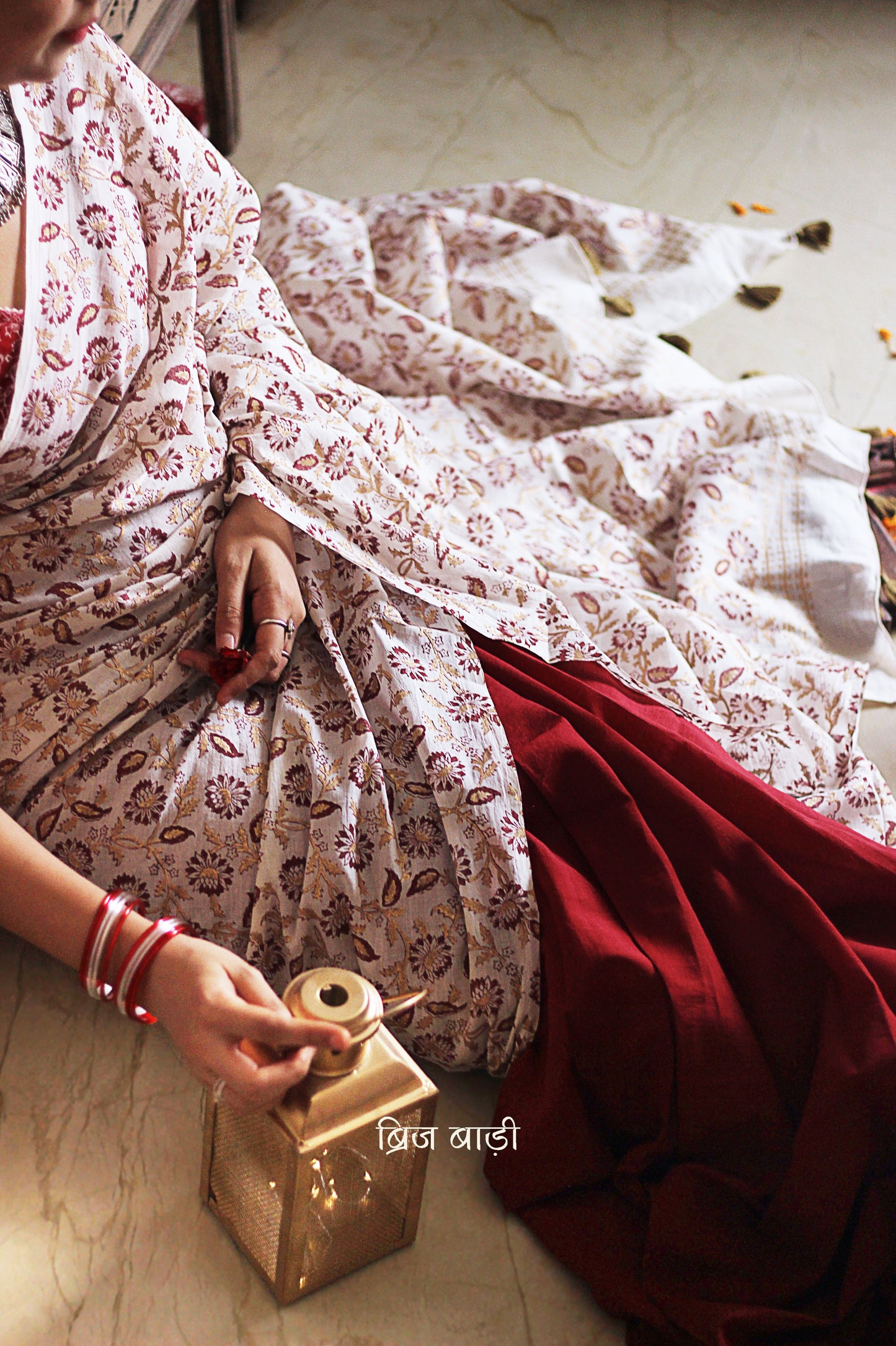 Deep red and off-white ombré handcrafted cotton saree by Brij Bari, made from soft, light-weight fabric for all-day comfort. Adorned with elegant floral hand block prints in subtle golden and red accents, this saree offers a versatile and graceful look for festive occasions. The pallu is enhanced with handcrafted olive green thread tassels, adding earthy detail to its festive charm. Comes with a free hand block printed blouse piece. A timeless fusion of artisanal beauty and breathable ease
