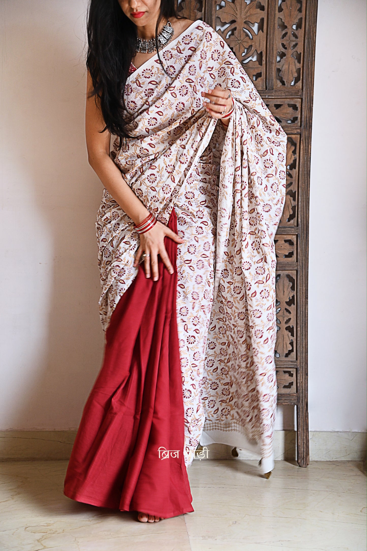 Deep red and off-white ombré handcrafted cotton saree by Brij Bari, made from soft, light-weight fabric for all-day comfort. Adorned with elegant floral hand block prints in subtle golden and red accents, this saree offers a versatile and graceful look for festive occasions. The pallu is enhanced with handcrafted olive green thread tassels, adding earthy detail to its festive charm. Comes with a free hand block printed blouse piece. A timeless fusion of artisanal beauty and breathable ease
