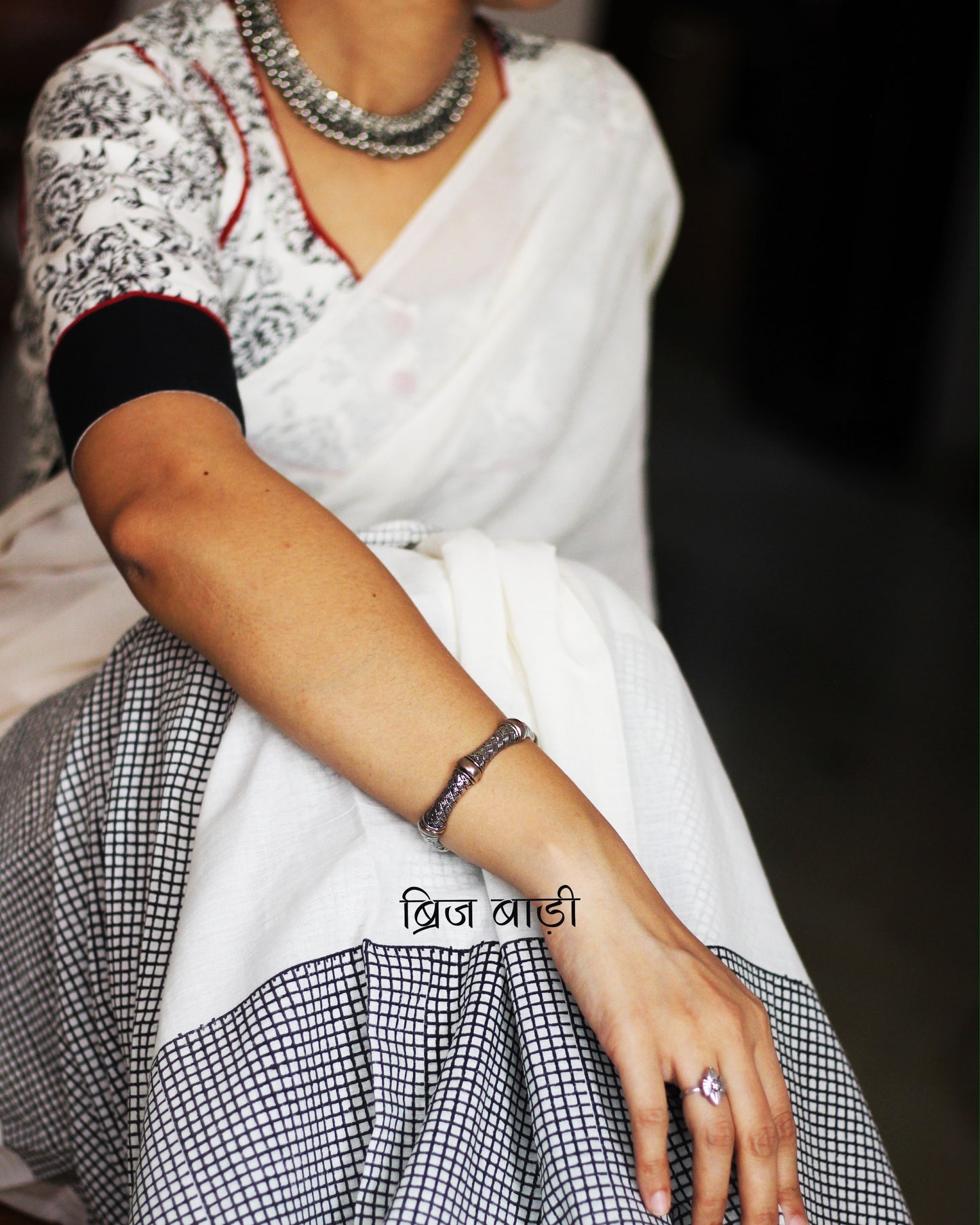 Off-white soft and light-weight cotton saree by Brij Bari, featuring a hand block printed check pattern on the skirt and geometrical pattern on the pallu. Designed for effortless everyday wear, this breathable, easy-drape saree brings together traditional craft with contemporary patterns. Finished with bright red handmade thread tassels on the pallu. Paired with a free hand block printed blouse piece that compliments the design perfectly. Offers free shipping pan India