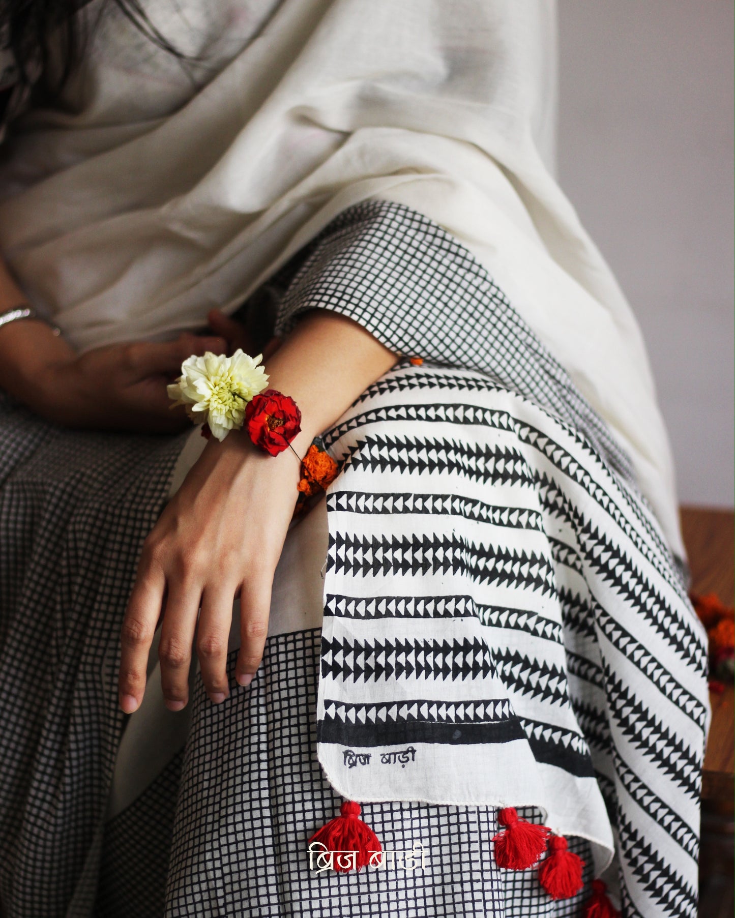 Off-white soft and light-weight cotton saree by Brij Bari, featuring a hand block printed check pattern on the skirt and geometrical pattern on the pallu. Designed for effortless everyday wear, this breathable, easy-drape saree brings together traditional craft with contemporary patterns. Finished with bright red handmade thread tassels on the pallu. Paired with a free hand block printed blouse piece that compliments the design perfectly. Offers free shipping pan India