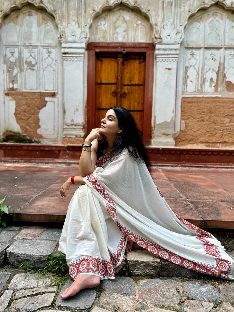 Sonal Singh a senior textile designer wearing our Parthivi saree. Off white soft and light-weight cotton saree by Brij Bari, featuring a delicate and intricate multicolour hand block printed border crafted by skilled artisans. Designed for all-day comfort and effortless style, this saree is detailed with olive green handmade thread tassels on the pallu. It comes with a free block printed blouse piece, making it a versatile pick for everyday wear, casual gatherings, and relaxed festive occasions.