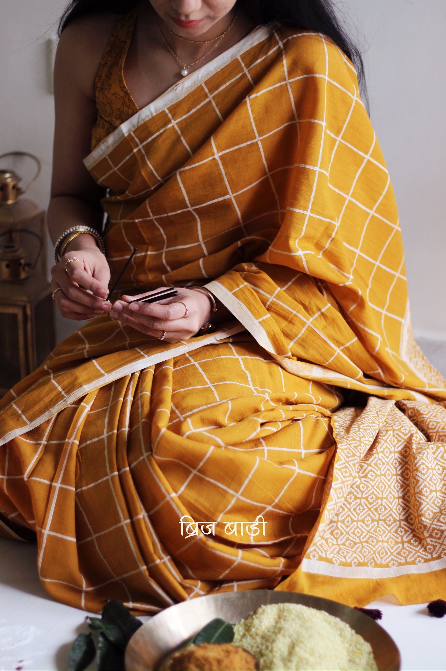 Yellow soft and light-weight cotton saree by Brij Bari, hand block printed in white with a classic check pattern on the body and a striking geometrical pattern on the pallu. Detailed with pink handmade thread tassels that add a charming, handcrafted touch. This saree comes with a free matching block printed blouse piece, offering a complete, artisanal look. A versatile, breathable saree perfect for everyday wear, casual outings, or semi-formal occasions, with free shipping pan India. Available in 2 colours