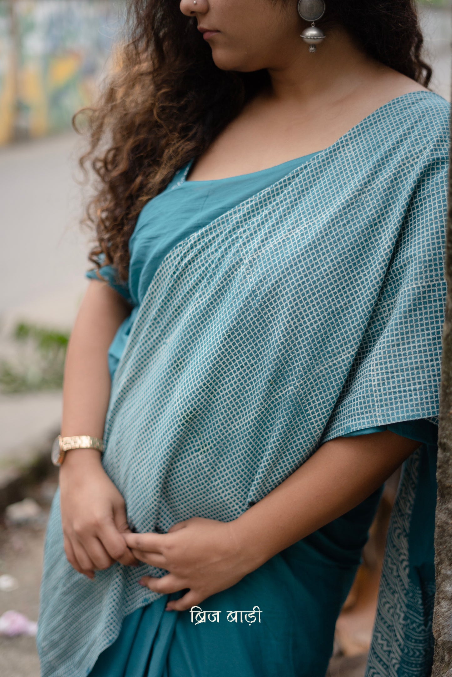 Teal blue soft and lightweight cotton saree by Brij Bari, hand block printed with a classic check pattern on the skirt and a geometric design in white on the pallu. Finished with handmade orange thread tassels on the pallu. Comes with a complimentary block printed cotton blouse piece. A versatile design that adds a pop of colour to your everyday wardrobe while offering breathable comfort and effortless style. Free shipping pan India.