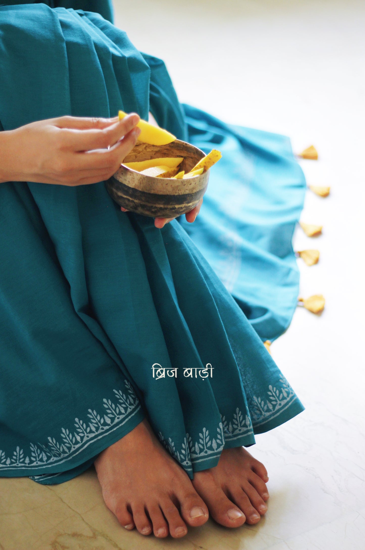 Teal blue soft and light-weight cotton saree by Brij Bari, designed for all-day comfort and effortless elegance. Detailed with a delicate hand block printed border in crisp white, creating a refined contrast. The saree is finished with orange handmade thread tassels on the pallu, adding a subtle pop of colour. Comes with a free matching block printed blouse piece. Ideal for everyday wear, office, casual outings, or light festive occasions, with free shipping pan India.