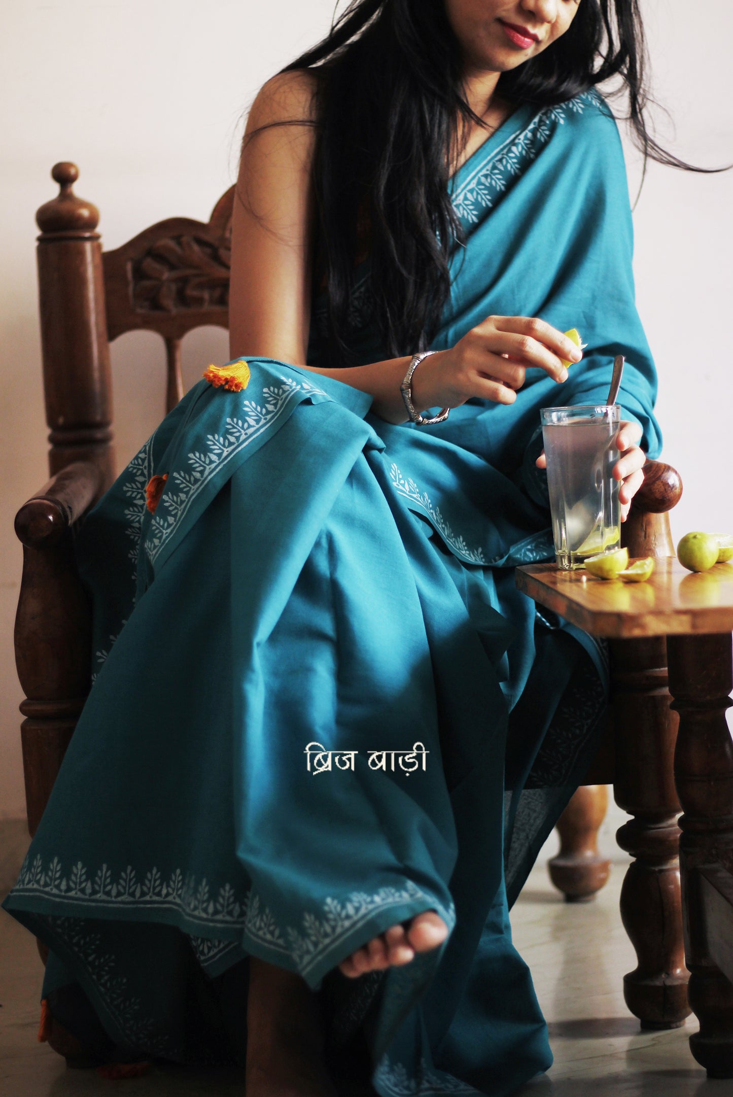 Teal blue soft and light-weight cotton saree by Brij Bari, designed for all-day comfort and effortless elegance. Detailed with a delicate hand block printed border in crisp white, creating a refined contrast. The saree is finished with orange handmade thread tassels on the pallu, adding a subtle pop of colour. Comes with a free matching block printed blouse piece. Ideal for everyday wear, office, casual outings, or light festive occasions, with free shipping pan India.