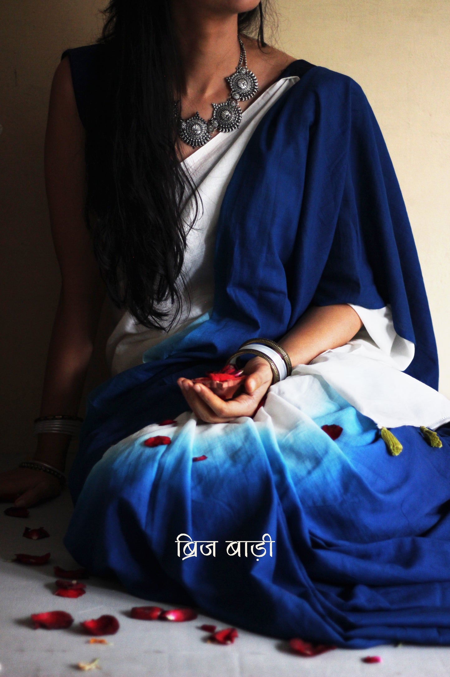 Deep Blue and off-white ombré soft cotton saree by Brij Bari, crafted for effortless elegance and all-day comfort. The subtle blend of tones adds fluidity and grace to the drape, making it perfect for both everyday wear and special occasions. The pallu is adorned with handcrafted light green thread tassels, lending a warm, artisanal touch. It comes with a free hand block printed blouse piece that complements the saree’s minimal yet striking aesthetic. Available in 8 beautiful colour options