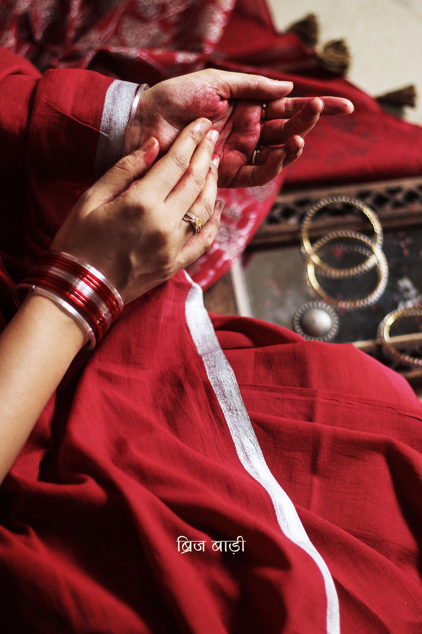 Deep red light-weight cotton saree by Brij Bari, featuring an intricately hand block printed floral pattern in gold and silver on the pallu. The saree is designed with a minimalist border for a timeless appeal, and the pallu is adorned with handcrafted olive green thread tassels that add a unique, earthy contrast. A versatile and comfortable pick for the festive season, it comes with a free matching hand block printed blouse piece. Thoughtfully crafted for elegance, ease, and tradition.