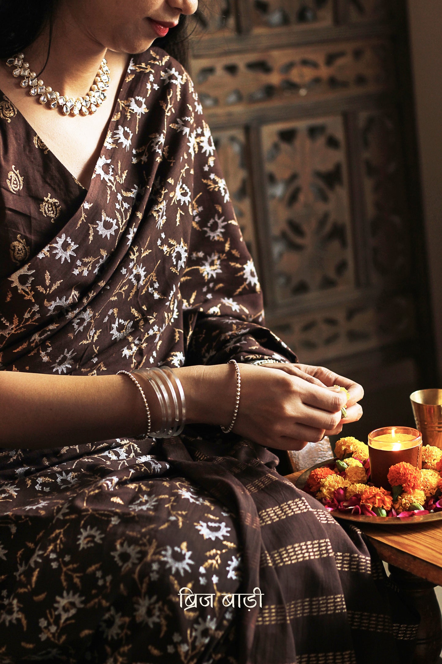 Brown soft cotton saree by Brij Bari, adorned with an abstract floral hand block print in elegant shades of gold and silver, lending it a refined festive charm. Crafted from breathable, light-weight cotton, the saree is accented with handcrafted mustard thread tassels on the pallu for a warm, artisanal finish. It comes with a free hand block printed blouse piece that complements the overall design. Ideal for festive occasions, this saree blends traditional techniques with modern aesthetics