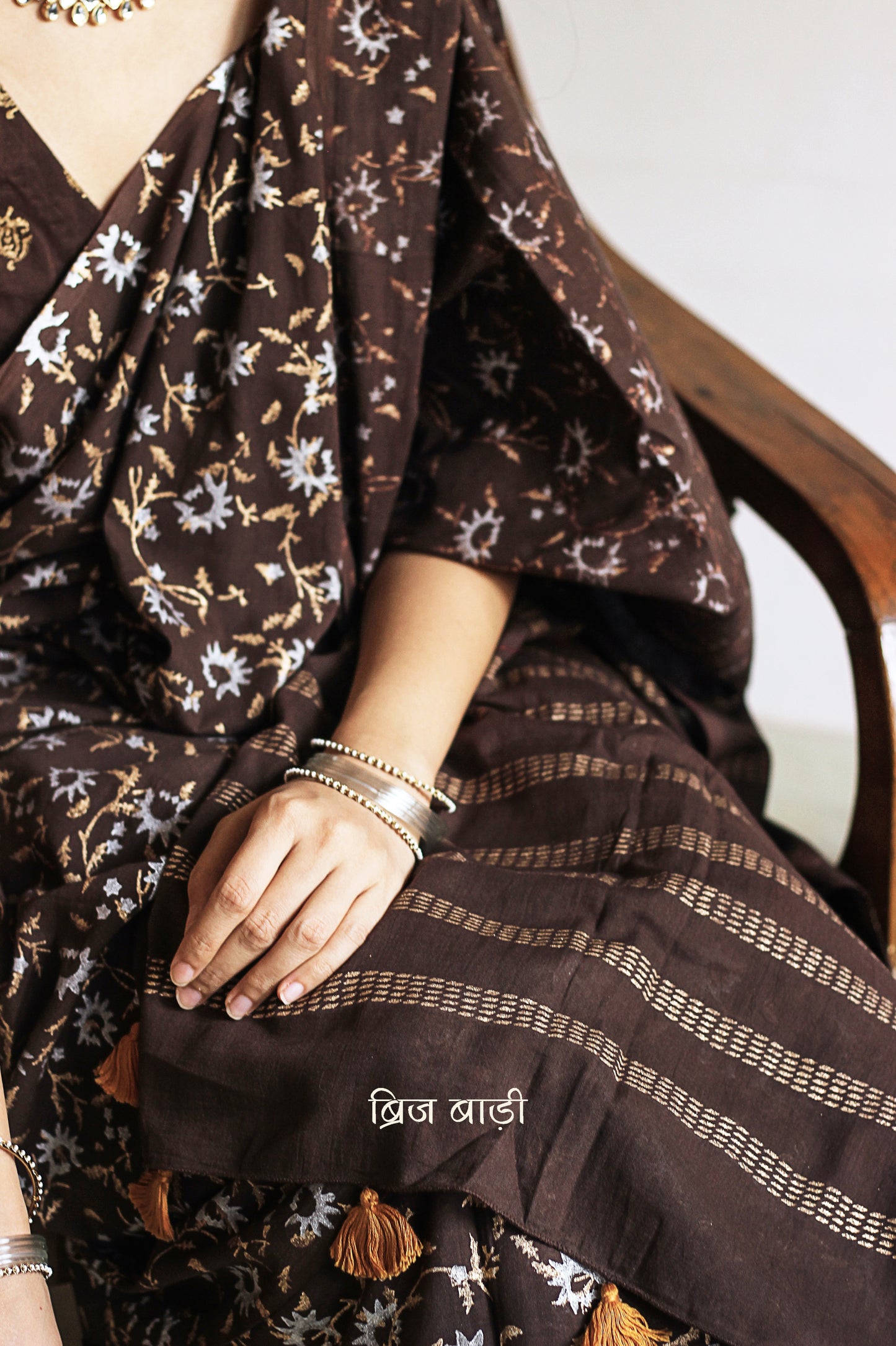 Brown soft cotton saree by Brij Bari, adorned with an abstract floral hand block print in elegant shades of gold and silver, lending it a refined festive charm. Crafted from breathable, light-weight cotton, the saree is accented with handcrafted mustard thread tassels on the pallu for a warm, artisanal finish. It comes with a free hand block printed blouse piece that complements the overall design. Ideal for festive occasions, this saree blends traditional techniques with modern aesthetics