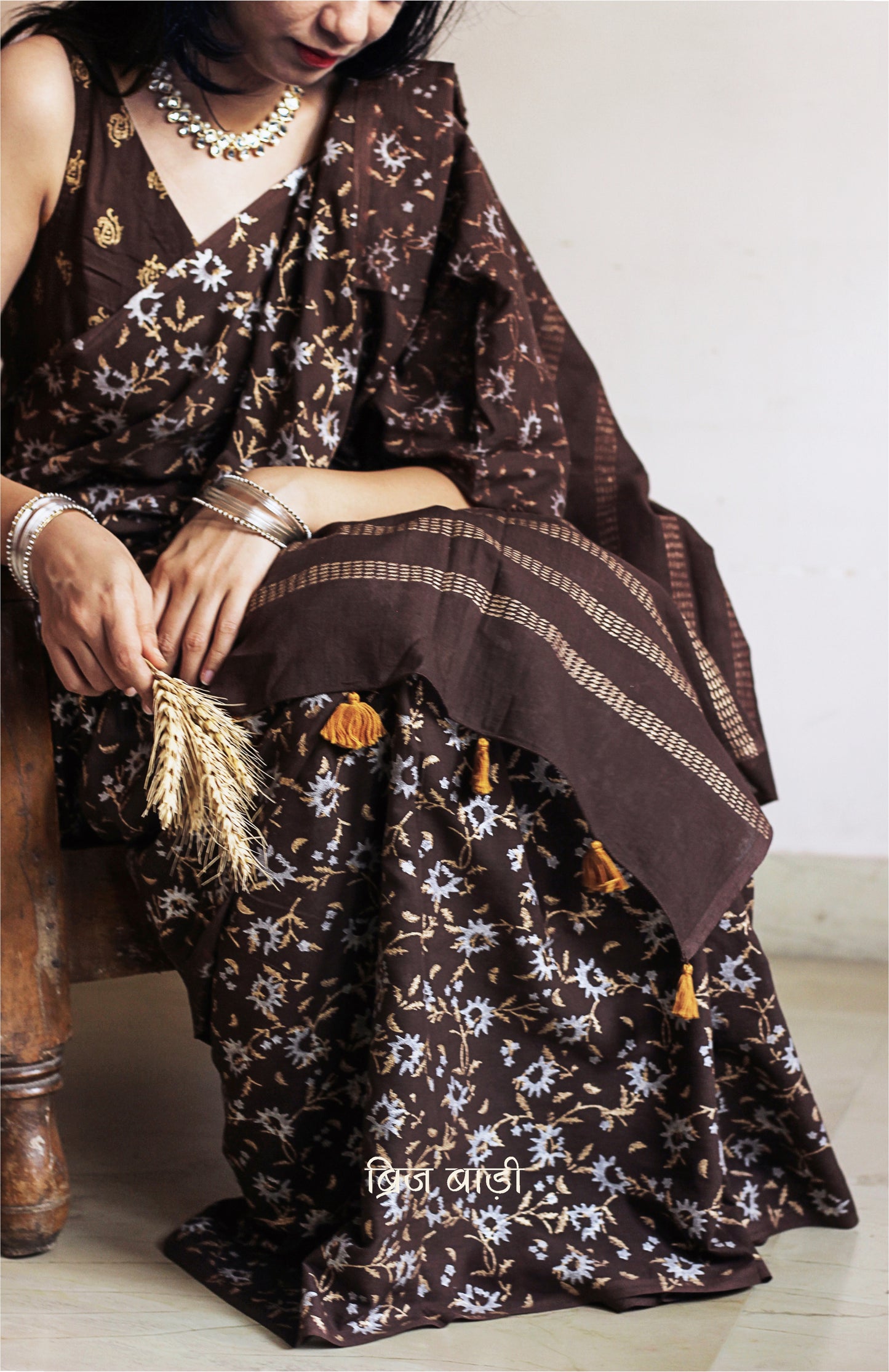 Brown soft cotton saree by Brij Bari, adorned with an abstract floral hand block print in elegant shades of gold and silver, lending it a refined festive charm. Crafted from breathable, light-weight cotton, the saree is accented with handcrafted mustard thread tassels on the pallu for a warm, artisanal finish. It comes with a free hand block printed blouse piece that complements the overall design. Ideal for festive occasions, this saree blends traditional techniques with modern aesthetics
