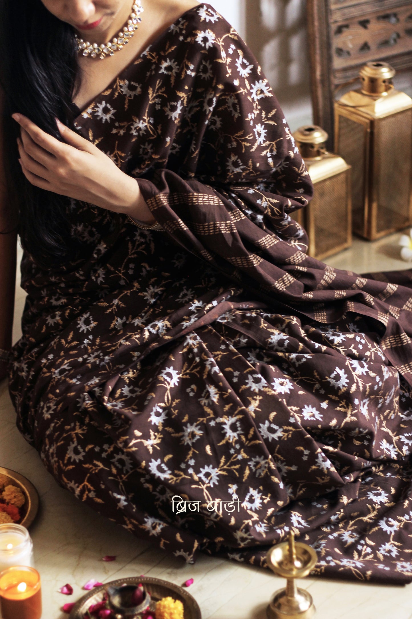 Brown soft cotton saree by Brij Bari, adorned with an abstract floral hand block print in elegant shades of gold and silver, lending it a refined festive charm. Crafted from breathable, light-weight cotton, the saree is accented with handcrafted mustard thread tassels on the pallu for a warm, artisanal finish. It comes with a free hand block printed blouse piece that complements the overall design. Ideal for festive occasions, this saree blends traditional techniques with modern aesthetics