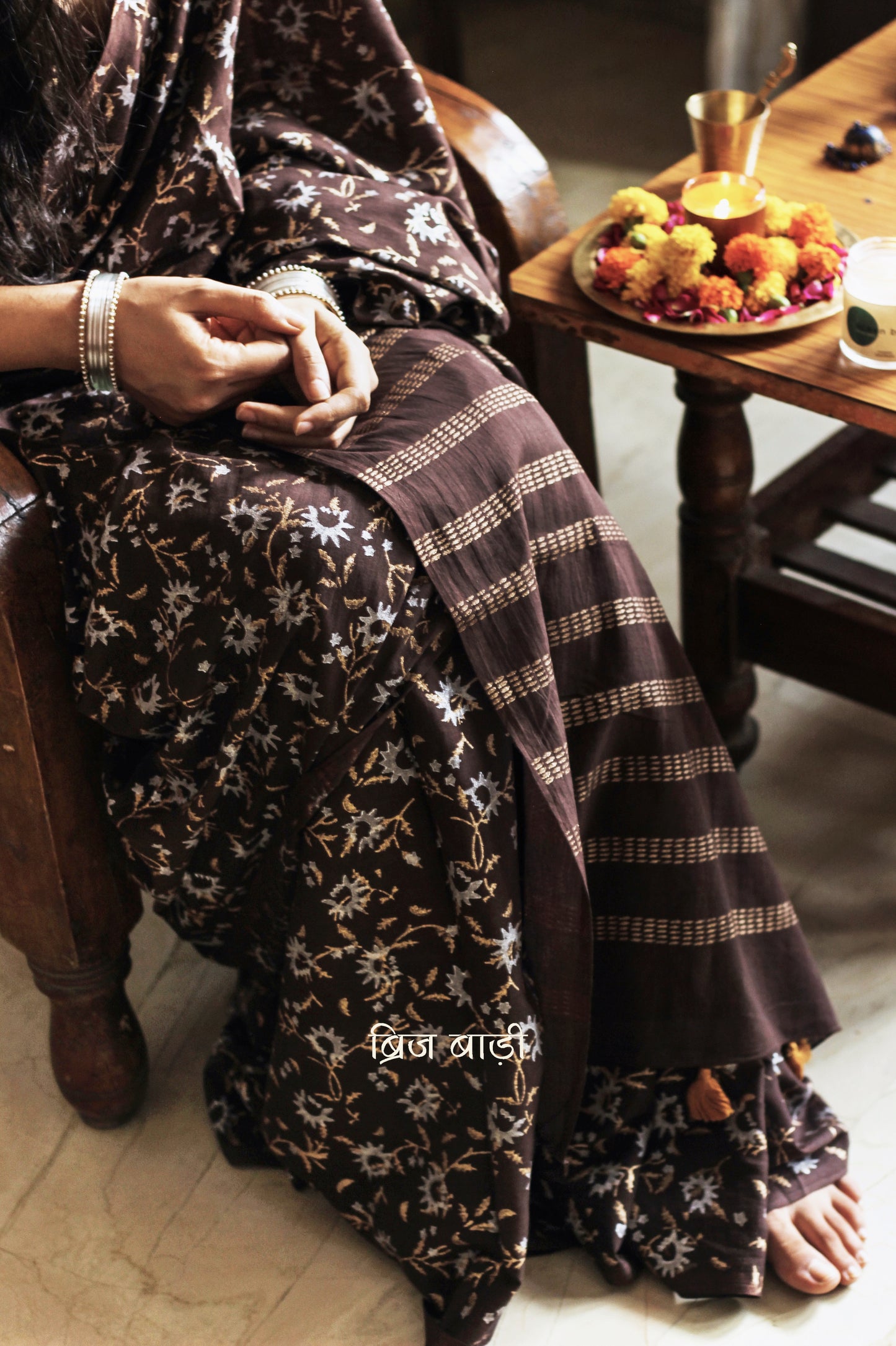 Brown soft cotton saree by Brij Bari, adorned with an abstract floral hand block print in elegant shades of gold and silver, lending it a refined festive charm. Crafted from breathable, light-weight cotton, the saree is accented with handcrafted mustard thread tassels on the pallu for a warm, artisanal finish. It comes with a free hand block printed blouse piece that complements the overall design. Ideal for festive occasions, this saree blends traditional techniques with modern aesthetics