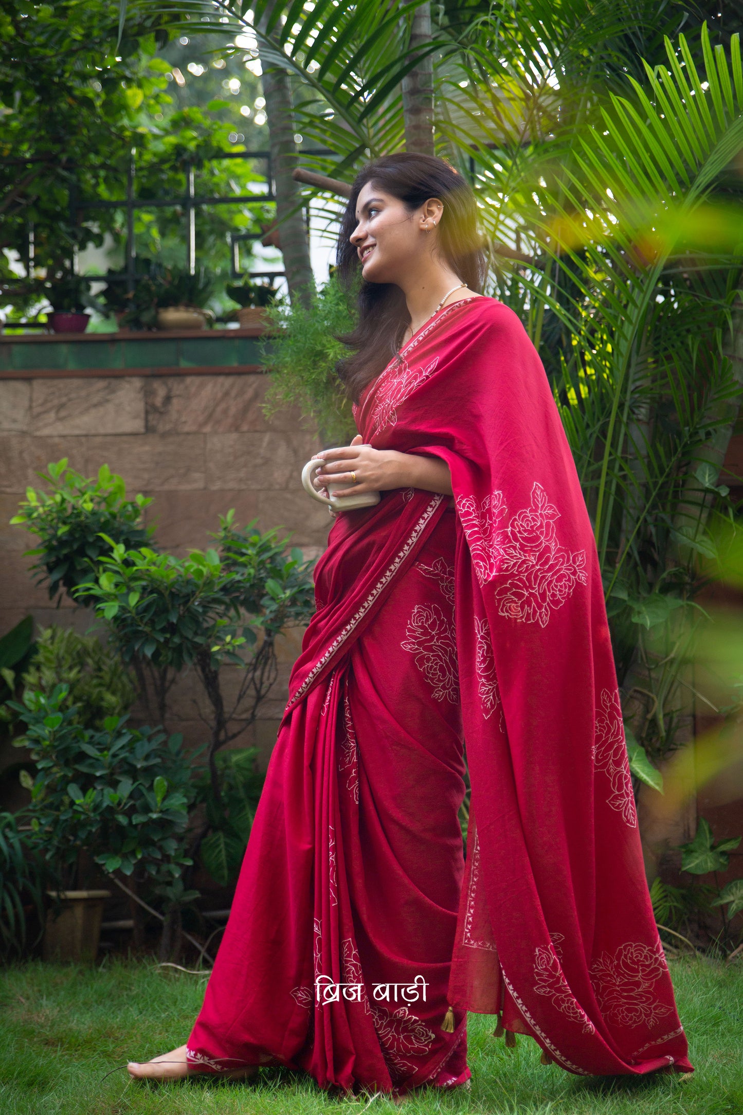Deep red buttery soft and lightweight cotton saree by Brij Bari, hand block printed with delicate white rose motifs for a refined, artisanal touch. The pallu is finished with olive green handmade thread tassels that add a subtle contrast and handcrafted charm. Comes with a free coordinated block printed blouse piece. Designed for all-day comfort and understated elegance, this saree is a versatile pick for everyday wear or casual occasions. Free shipping pan India.