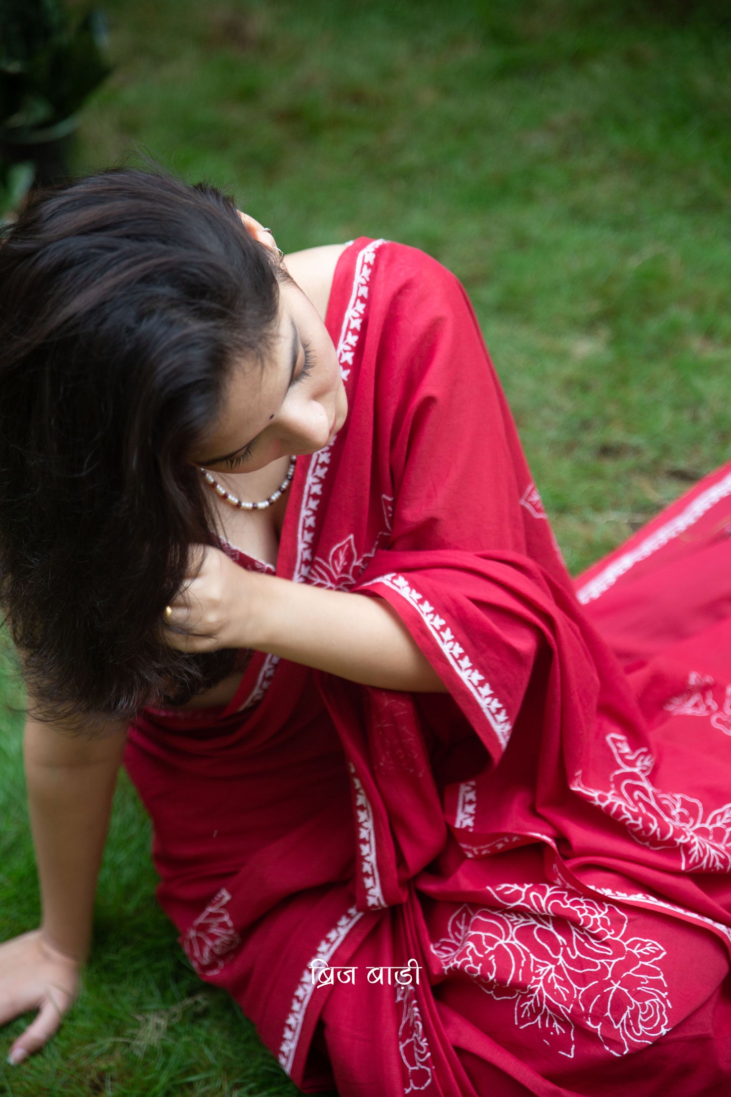 Deep red buttery soft and lightweight cotton saree by Brij Bari, hand block printed with delicate white rose motifs for a refined, artisanal touch. The pallu is finished with olive green handmade thread tassels that add a subtle contrast and handcrafted charm. Comes with a free coordinated block printed blouse piece. Designed for all-day comfort and understated elegance, this saree is a versatile pick for everyday wear or casual occasions. Free shipping pan India.