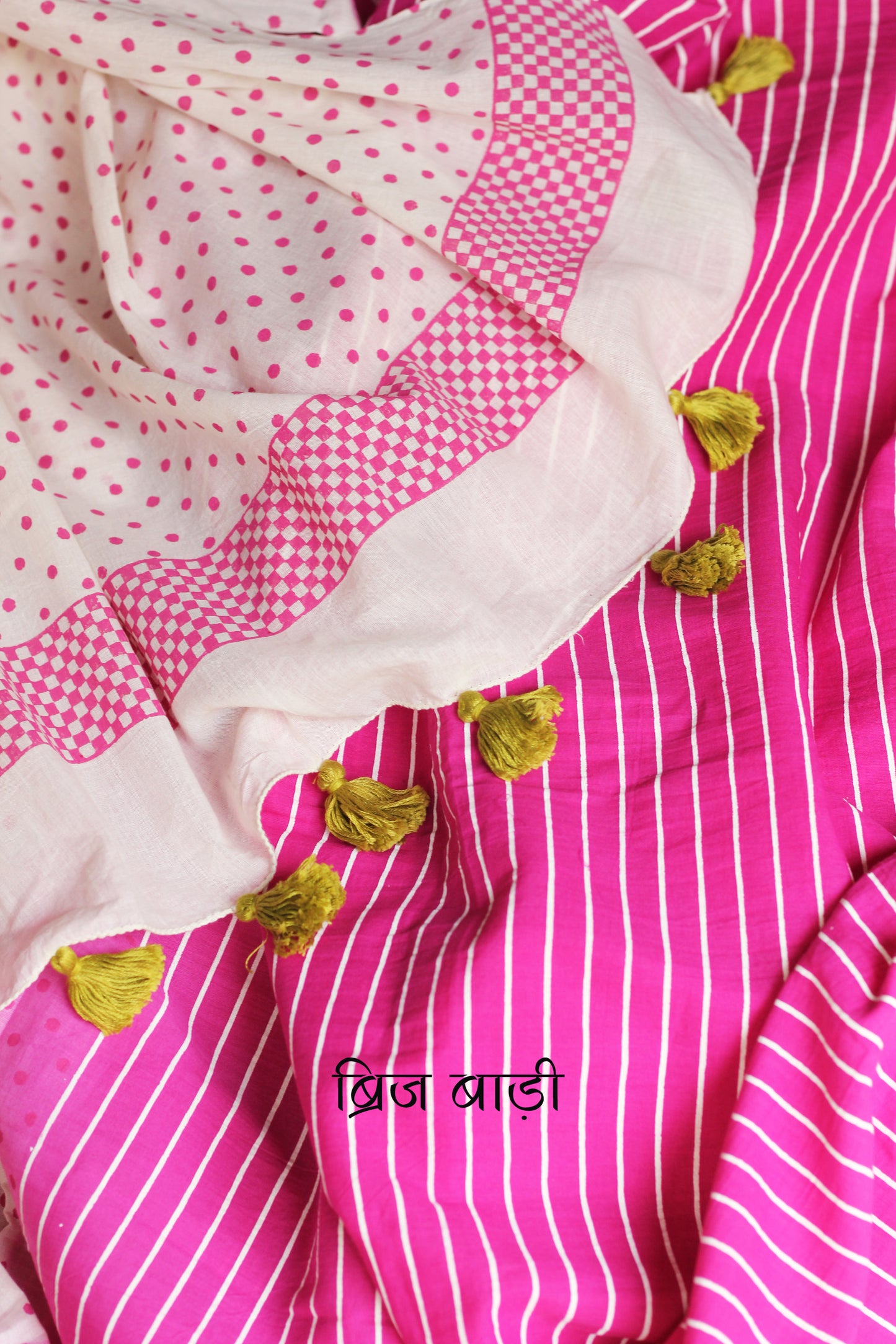 Pink & Off White ombre soft cotton saree by Brij Bari, featuring a bold and striking hand block printed pattern of stripes and polka dots for a modern, playful twist. Handcrafted from breathable, light-weight cotton, the saree drapes effortlessly—ideal for both everyday wear and special occasions. Finished with handcrafted light blue thread tassels on the pallu, adding an artisanal touch of charm. It comes with a free hand block printed blouse piece that compliments the print and palette.