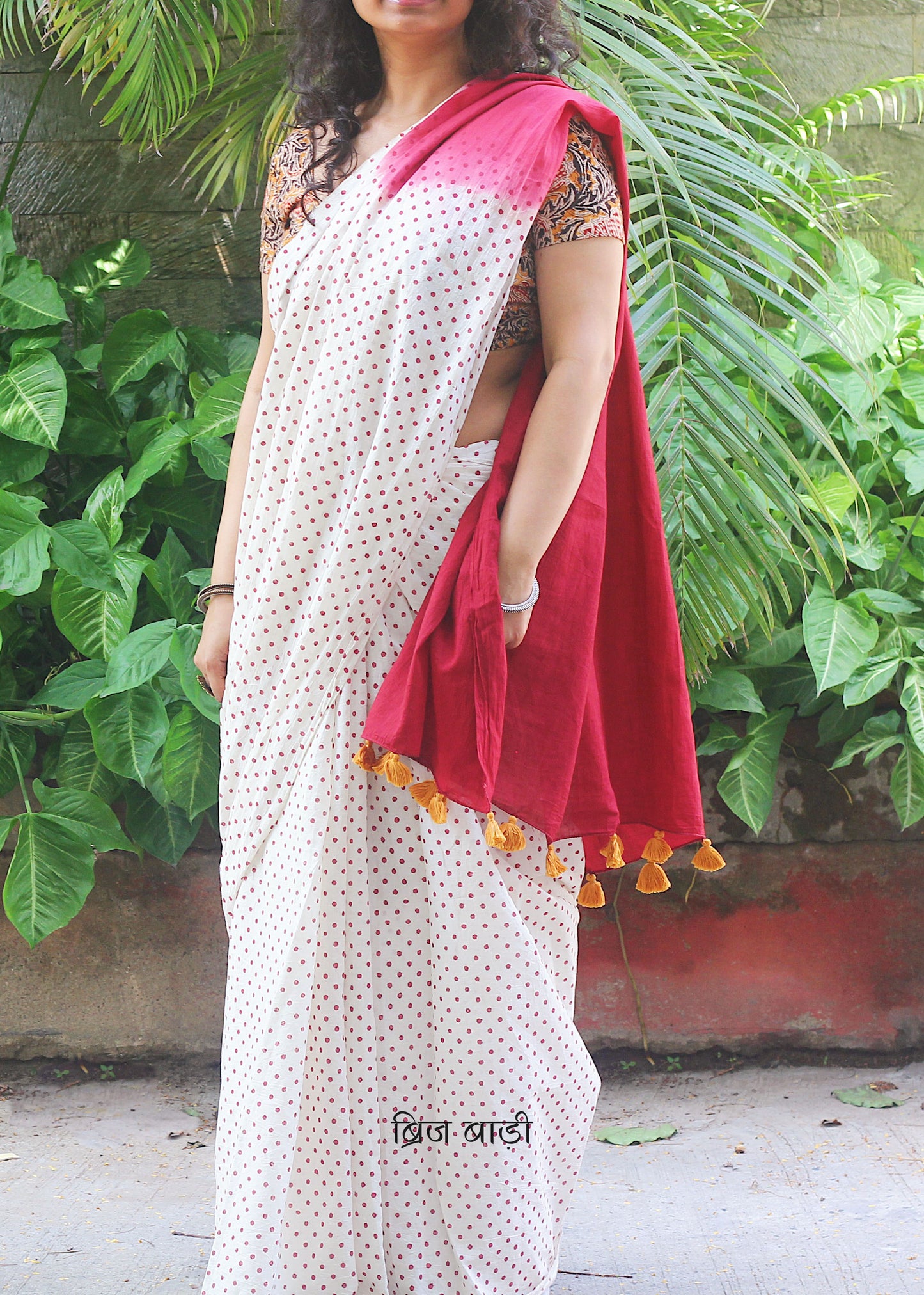 Off-white soft and light-weight cotton saree by Brij Bari, featuring deep red ombre pallu and small retro-style polka dot hand block prints. Accented with handcrafted mustard thread tassels on the pallu for a touch of artisanal charm. Includes a free matching hand block printed blouse piece. A timeless piece combining elegance, tradition, and comfort—crafted by Brij Bari’s skilled artisans.