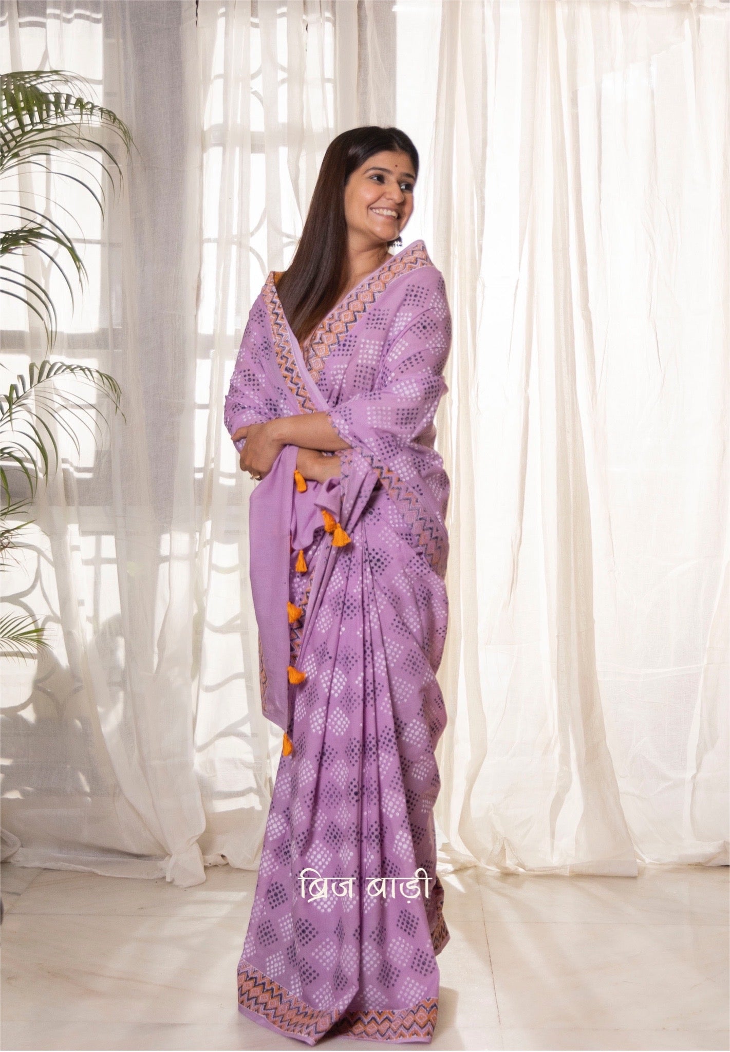 Lavender buttery soft and light-weight cotton saree by Brij Bari, featuring a playful polka dot pattern hand block printed in blue and yellow on the pallu. The saree is detailed with orange handmade thread tassels on the pallu, adding a pop of color. It comes with a free block printed blouse piece, making it a versatile option for everyday wear and casual occasions. Designed for all-day comfort and style, with free shipping available pan India.
