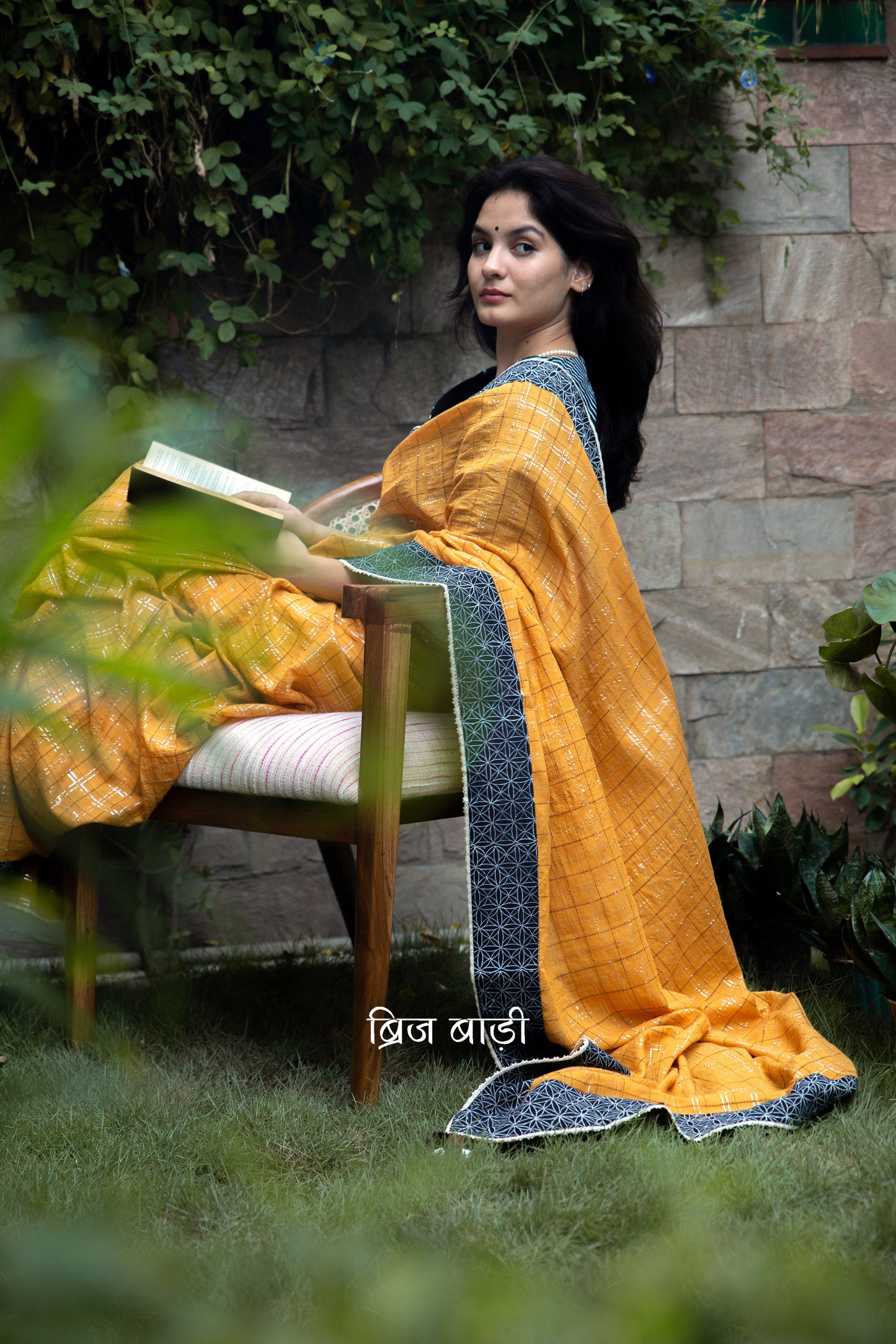 Ochre yellow cotton saree by Brij Bari crafted with lurex and thread detailing for a subtle shimmer. It is beautifully finished with a contrasting hand block printed black border & delicate crochet lace. The pallu is adorned with handmade purple & pink thread tassels accented with decorative sea shells on the corner adding a festive charm. An elegant pick for celebrations & special occasions, saree is designed to make heads turn while ensuring all-day comfort. Comes with free block printed blouse piece