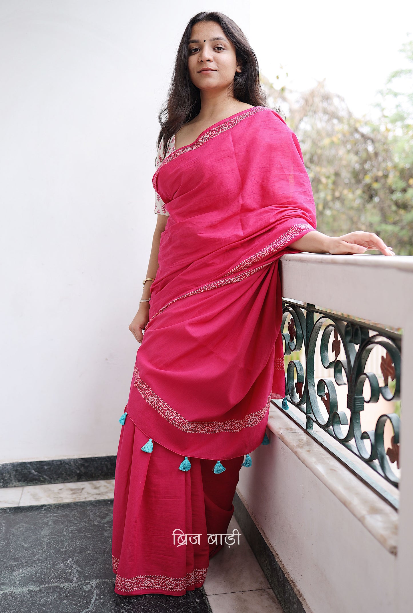 Pink soft and light-weight cotton saree by Brij Bari witha simple & elegant hand block printed border in classic white for a fresh, minimal appeal. Crafted from breathable, airy cotton, this saree is perfect for everyday wear — easy to drape, comfortable for the summer, and effortlessly stylish for work or casual outings. The pallu is finished with striking red handmade thread tassels, adding a handcrafted artisanal touch. Comes with a free hand block printed blouse piece.