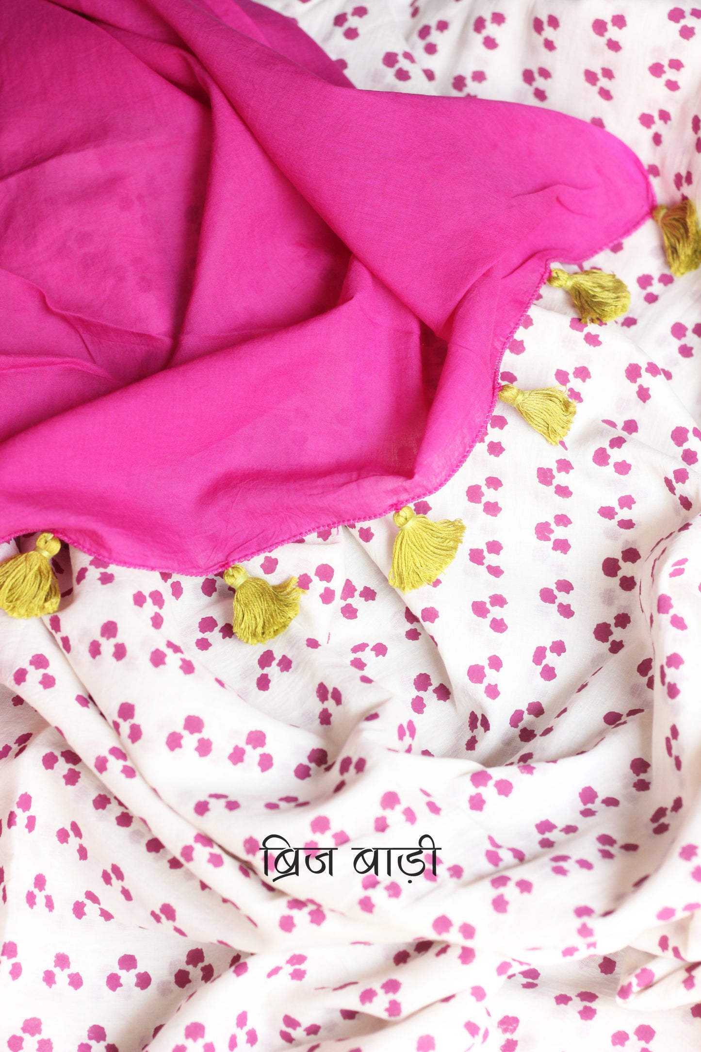 Off-white soft and light-weight cotton saree by Brij Bari, featuring a pink ombré palla that adds a graceful gradient to the drape. Hand block printed with a playful triple polka dot pattern all over, this saree blends charm with simplicity. The pallu is finished with handcrafted light green thread tassels for a subtle contrast. Ideal for everyday elegance and warm-weather comfort, it comes with a free hand block printed blouse piece that perfectly complements the saree.