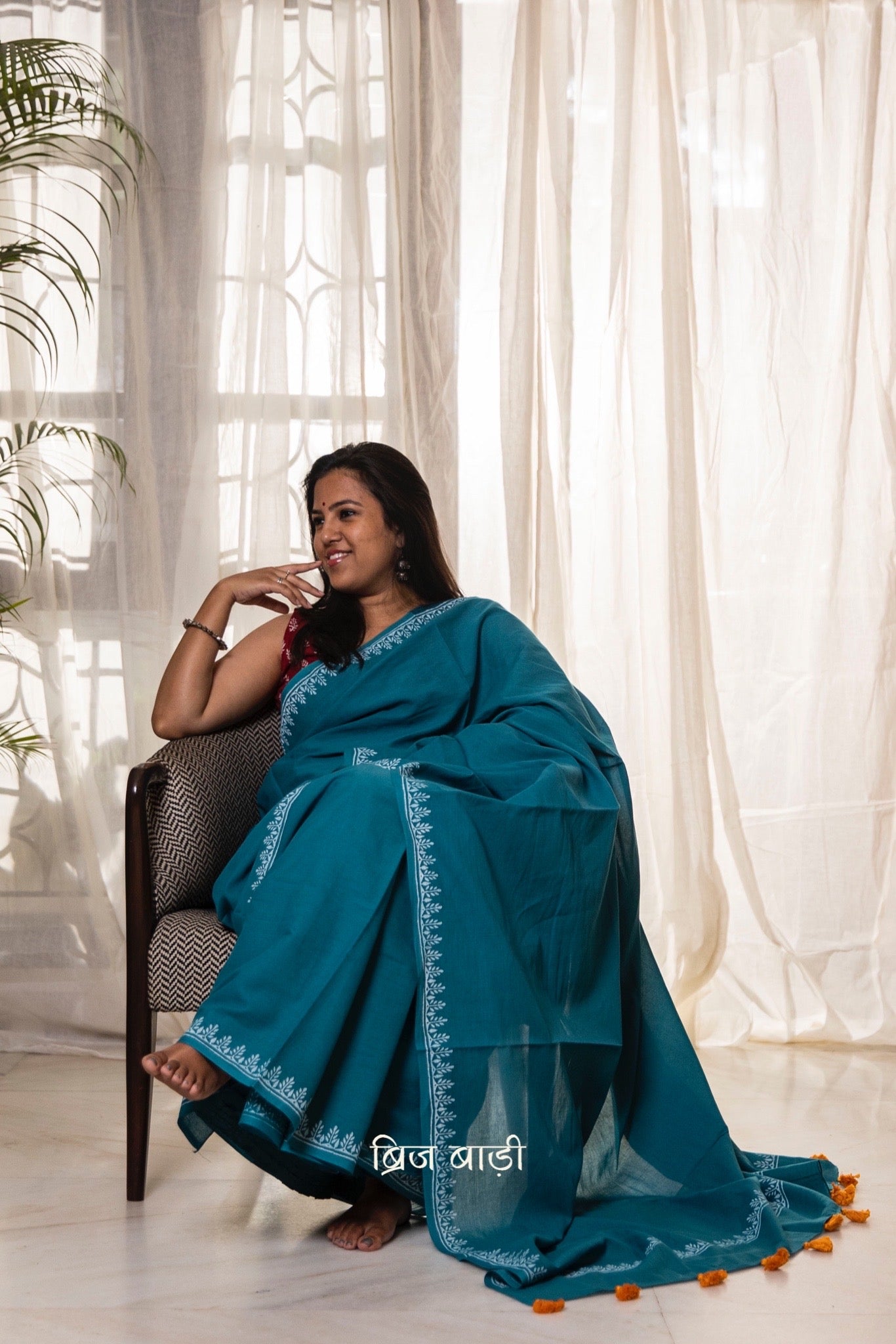 Teal blue soft and light-weight cotton saree by Brij Bari, designed for all-day comfort and effortless elegance. Detailed with a delicate hand block printed border in crisp white, creating a refined contrast. The saree is finished with orange handmade thread tassels on the pallu, adding a subtle pop of colour. Comes with a free matching block printed blouse piece. Ideal for everyday wear, office, casual outings, or light festive occasions, with free shipping pan India.