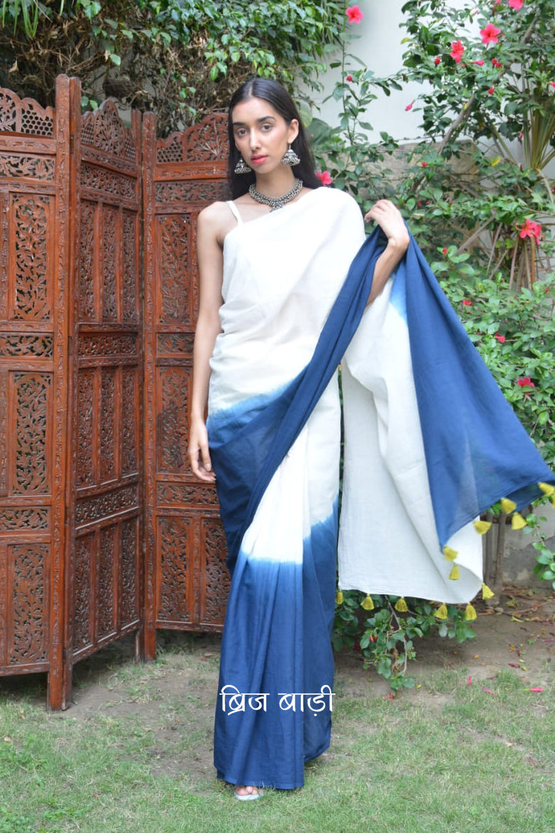 Deep Blue & off-white ombré soft cotton saree by Brij Bari crafted for effortless elegance & all-day comfort. The subtle blend of tones adds fluidity & grace to the drape making it perfect for both everyday wear & special occasions. The pallu has handmade light green thread tassels lending an artisanal touch. It comes with a free hand block printed blouse piece that complements the saree’s minimal yet striking aesthetic. Available in 8 beautiful colour options, this saree is a timeless wardrobe essential