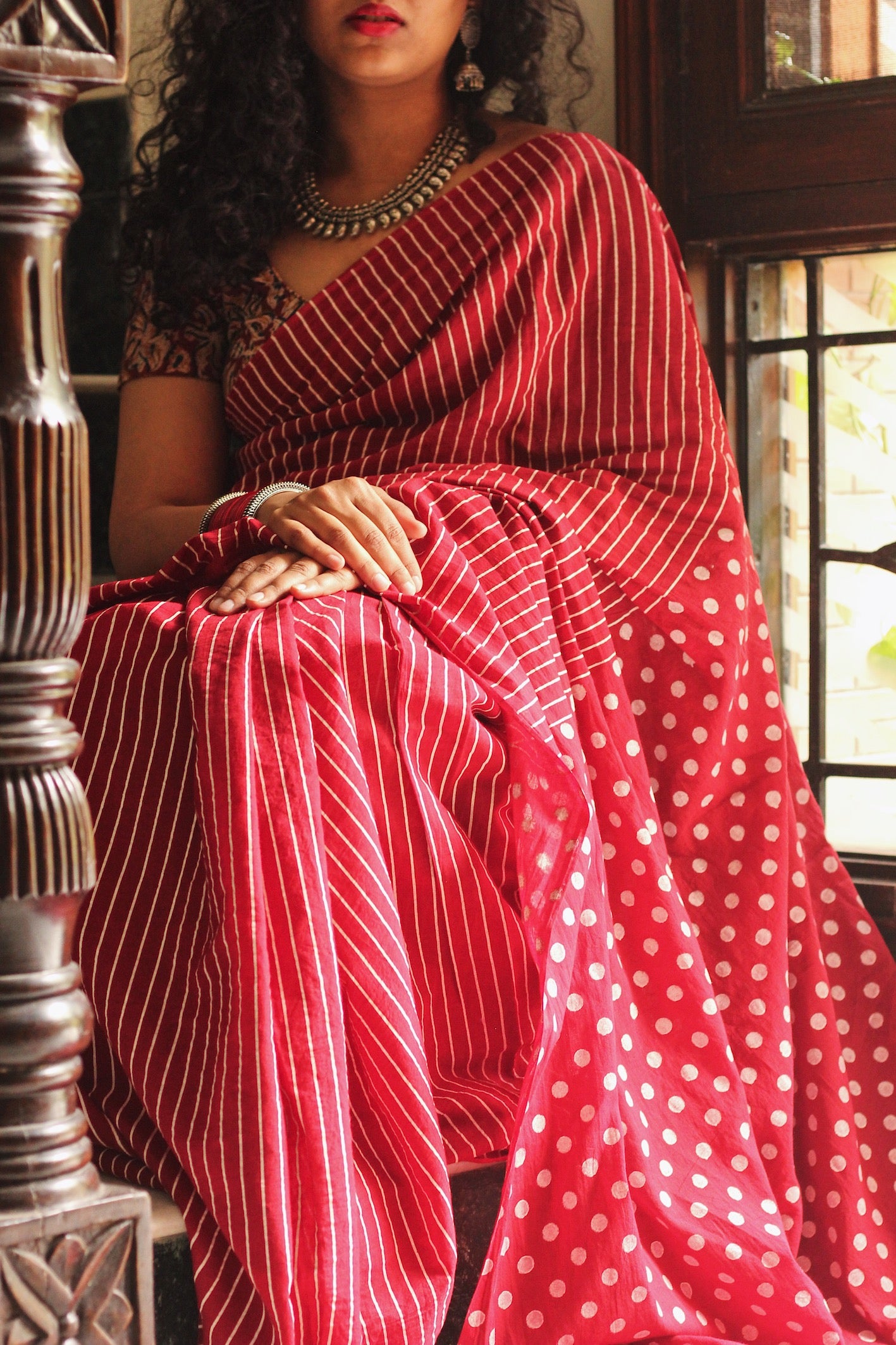 Red soft cotton saree by Brij Bari, featuring a bold and striking hand block printed pattern of stripes and polka dots for a modern, playful twist. Handcrafted from breathable, light-weight cotton, the saree drapes effortlessly—ideal for both everyday wear and special occasions. Finished with handcrafted olive green thread tassels on the pallu, adding an artisanal touch of charm. It comes with a free hand block printed blouse piece that complements the print and palette.