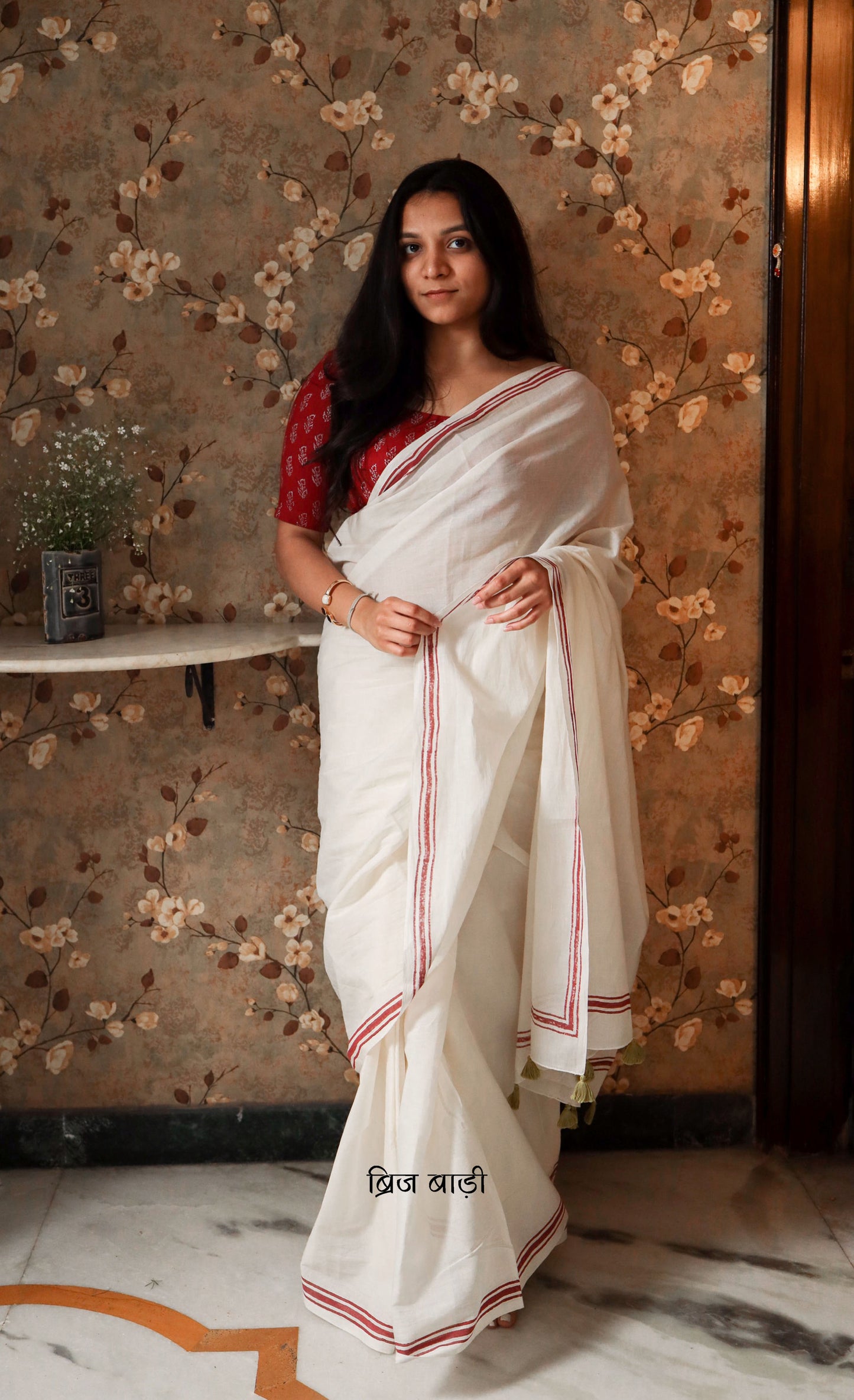 Off-white soft and light-weight cotton saree by Brij Bari with a simple and elegant hand block printed stripe pattern border in rich red. Designed for breathable comfort and effortless everyday style, this saree drapes beautifully for work, casual days or relaxed occasions. The pallu is finished with delicate light green handmade thread tassels adding a subtle artisanal detail. It comes with a free hand block printed blouse piece thoughtfully designed to complement the saree’s minimal design. Free Shipping