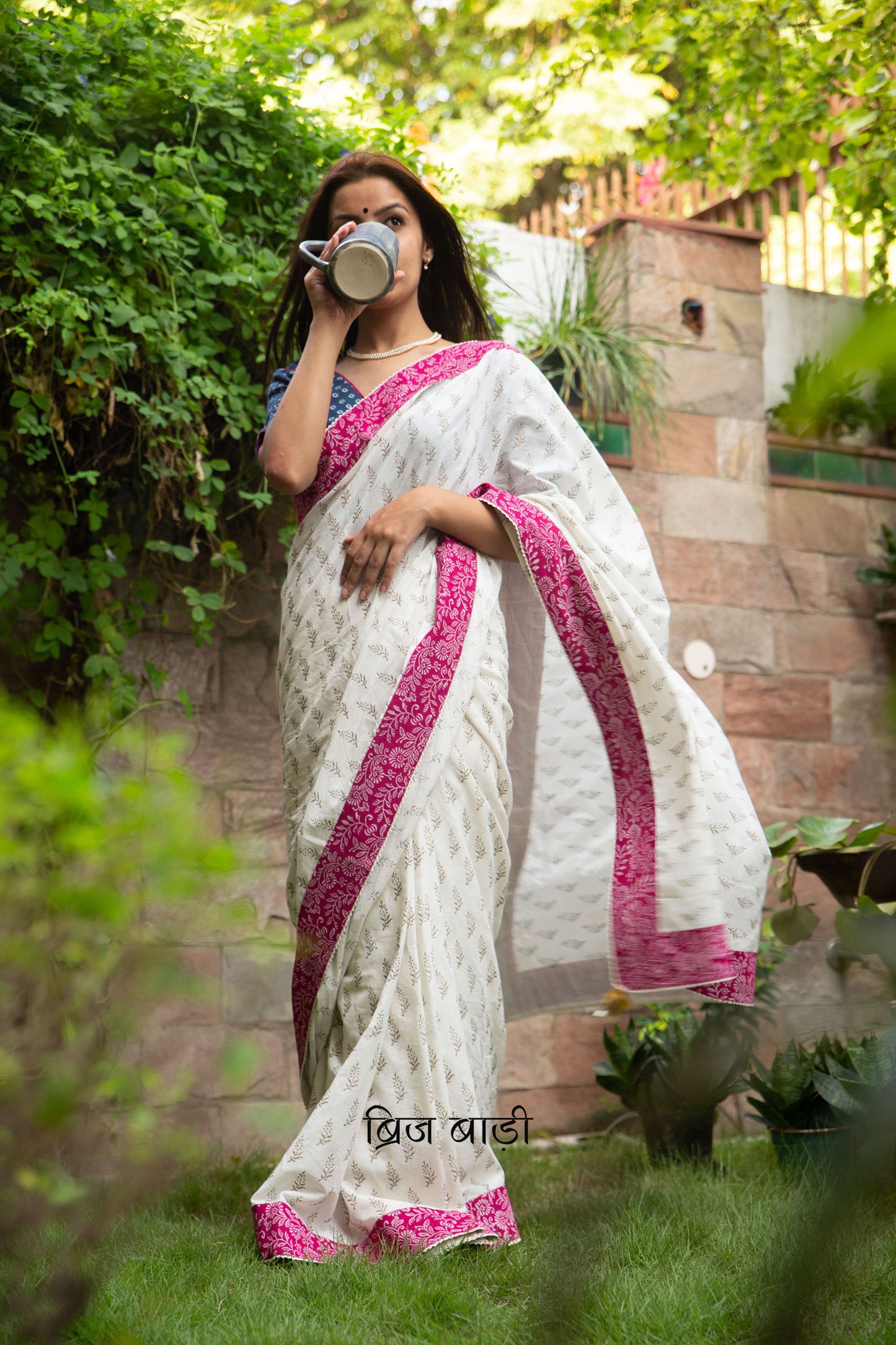 Off white soft cotton saree by Brij Bari hand block printed with intricate gold floral motifs & beautifully contrasted with a pink block printed border. Finished with delicate crochet detailing & adorned with yellow & light green handmade thread tassels accented with sea shells on pallu corner. Comes with matching block printed blouse piece. Perfect pick for festive or special occasions designed to make you stand out while staying effortlessly comfortable through long celebrations. Free shipping pan India