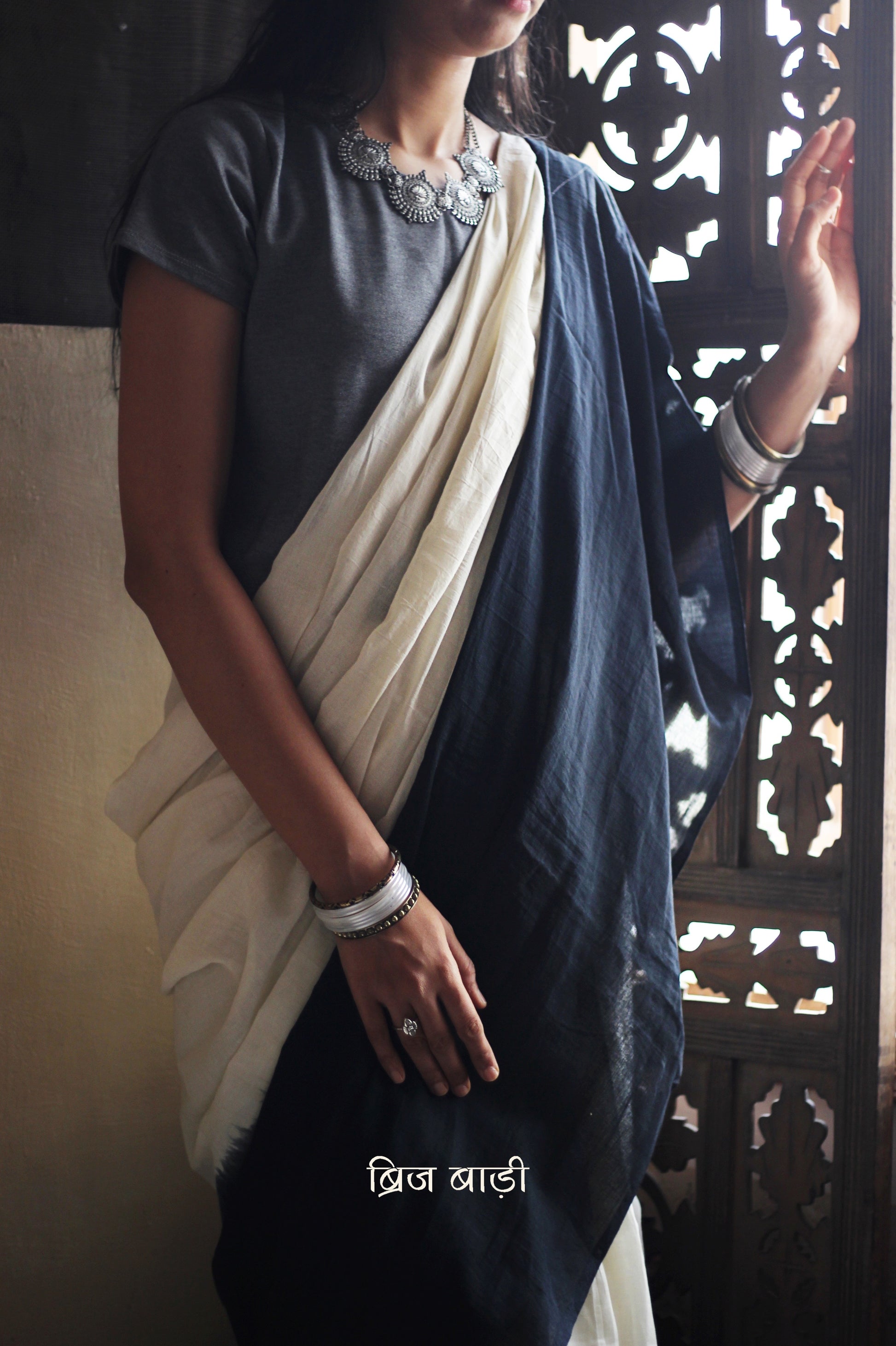 Black and off-white ombré soft cotton saree by Brij Bari, crafted for effortless elegance and all-day comfort. The subtle blend of tones adds fluidity and grace to the drape, making it perfect for both everyday wear and special occasions. The pallu is adorned with handcrafted pink thread tassels, lending a warm, artisanal touch. It comes with a free hand block printed blouse piece that complements the saree’s minimal yet striking aesthetic. Available in 8 beautiful colour options