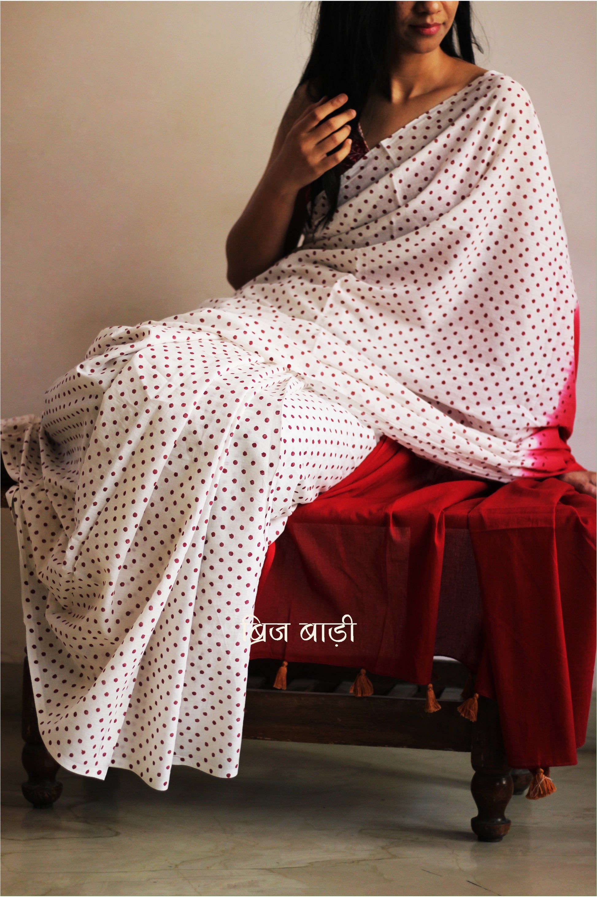 Off-white soft and light-weight cotton saree by Brij Bari, featuring deep red ombre pallu and small retro-style polka dot hand block prints. Accented with handcrafted mustard thread tassels on the pallu for a touch of artisanal charm. Includes a free matching hand block printed blouse piece. A timeless piece combining elegance, tradition, and comfort—crafted by Brij Bari’s skilled artisans.