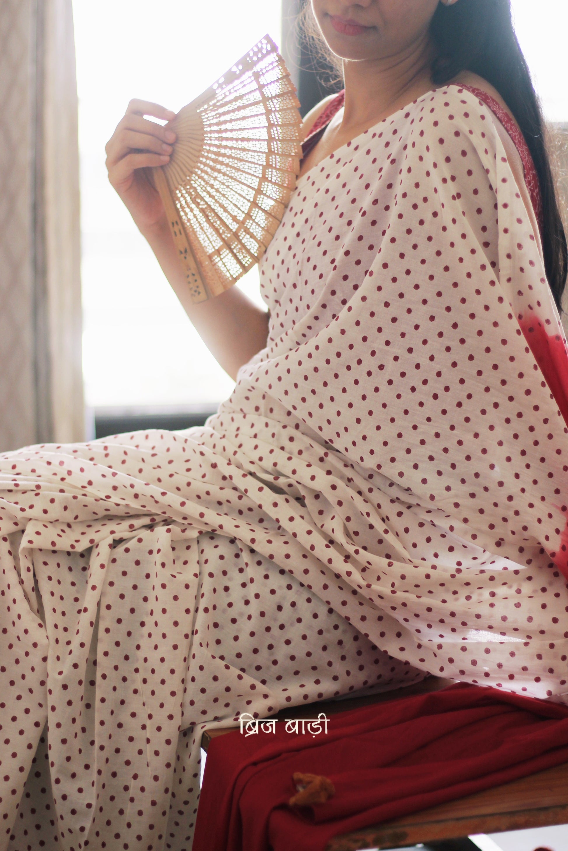 Off-white soft and light-weight cotton saree by Brij Bari, featuring deep red ombre pallu and small retro-style polka dot hand block prints. Accented with handcrafted mustard thread tassels on the pallu for a touch of artisanal charm. Includes a free matching hand block printed blouse piece. A timeless piece combining elegance, tradition, and comfort—crafted by Brij Bari’s skilled artisans.