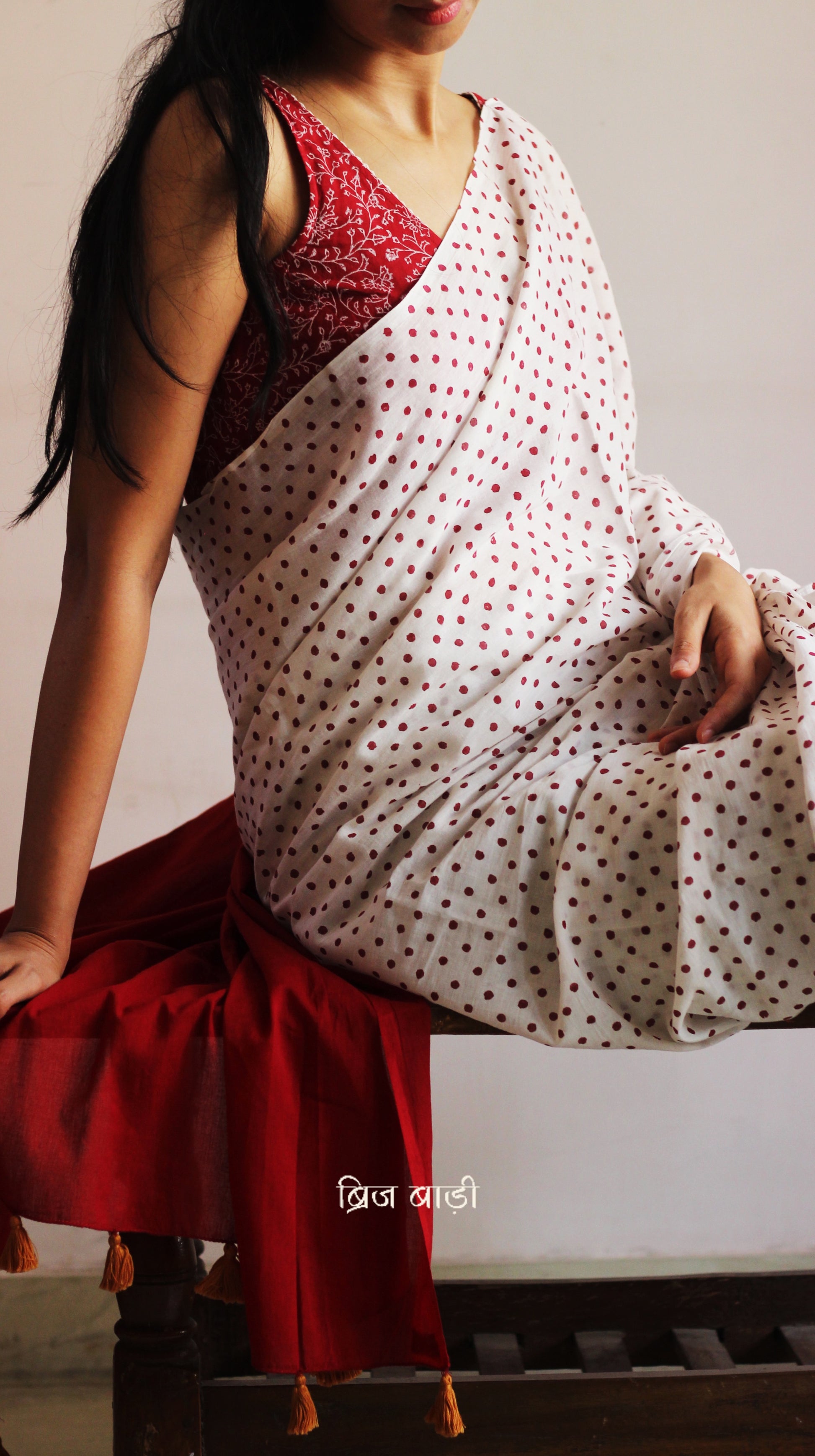 Off-white soft and light-weight cotton saree by Brij Bari, featuring deep red ombre pallu and small retro-style polka dot hand block prints. Accented with handcrafted mustard thread tassels on the pallu for a touch of artisanal charm. Includes a free matching hand block printed blouse piece. A timeless piece combining elegance, tradition, and comfort—crafted by Brij Bari’s skilled artisans.