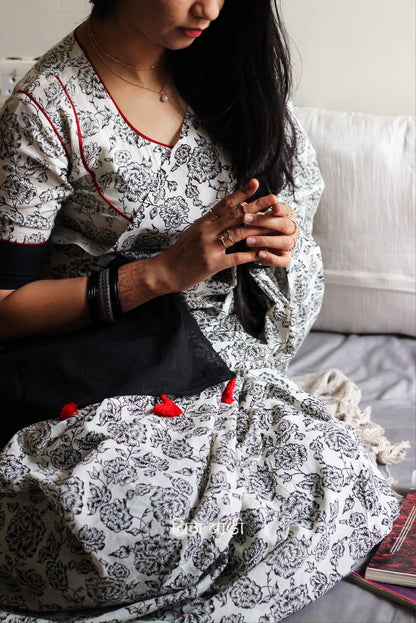 Off-white soft and light-weight cotton saree by Brij Bari, hand block printed with a delicate rose pattern for an elegant, understated everyday look. Crafted from breathable cotton, this saree ensures comfort and ease of wear, ideal for workdays, casual gatherings or daily summer dressing. The pallu is finished with bright red handmade thread tassels adding a traditional handcrafted detail to the look. Comes with a free hand block printed blouse piece designed to perfectly compliment the saree. 