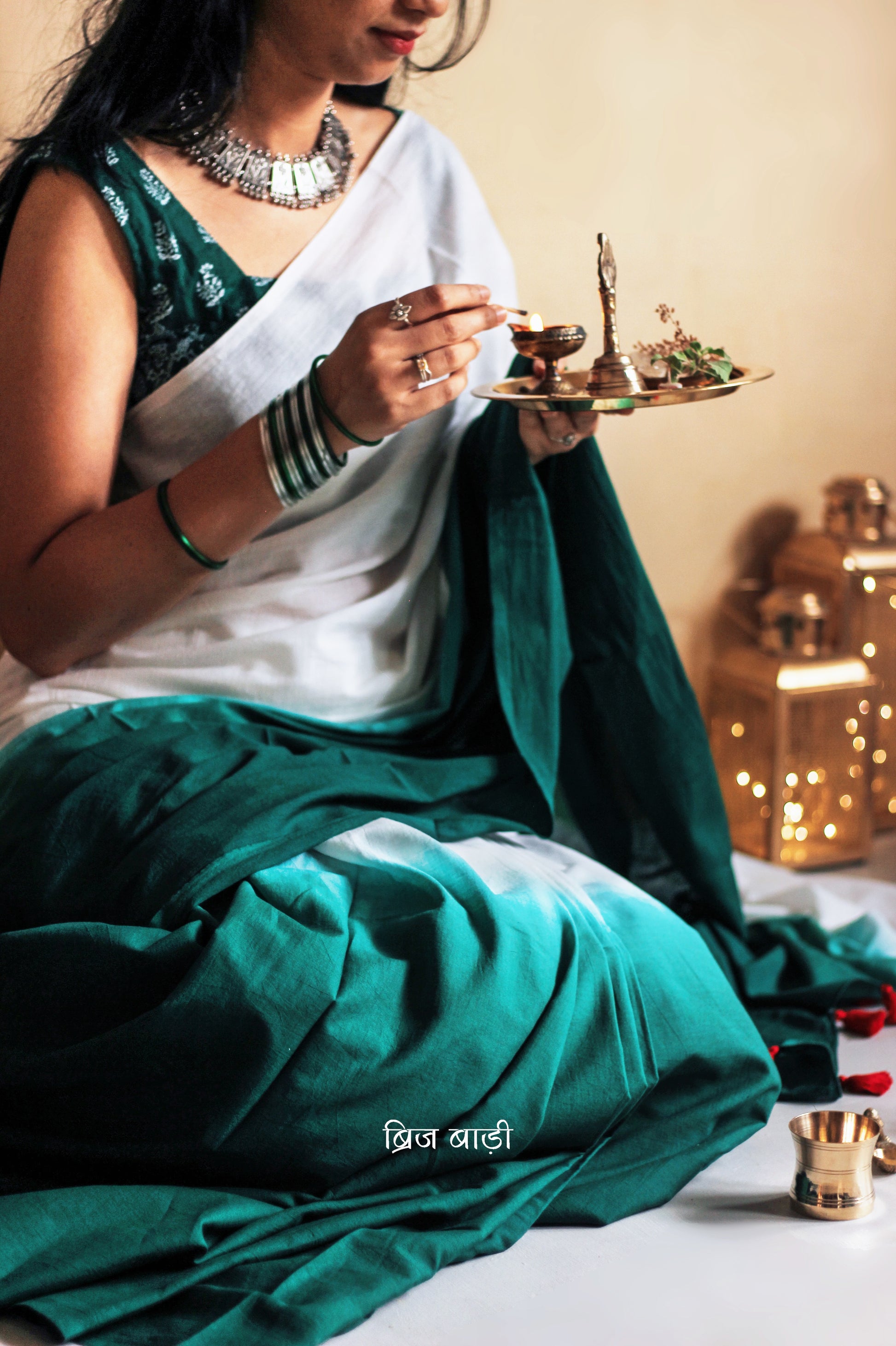 Dark Green and off-white ombré soft cotton saree by Brij Bari, crafted for effortless elegance and all-day comfort. The subtle blend of tones adds fluidity and grace to the drape, making it perfect for both everyday wear and special occasions. The pallu is adorned with handcrafted red thread tassels, lending a warm, artisanal touch. It comes with a free hand block printed blouse piece that complements the saree’s minimal yet striking aesthetic. Available in 8 beautiful colour options