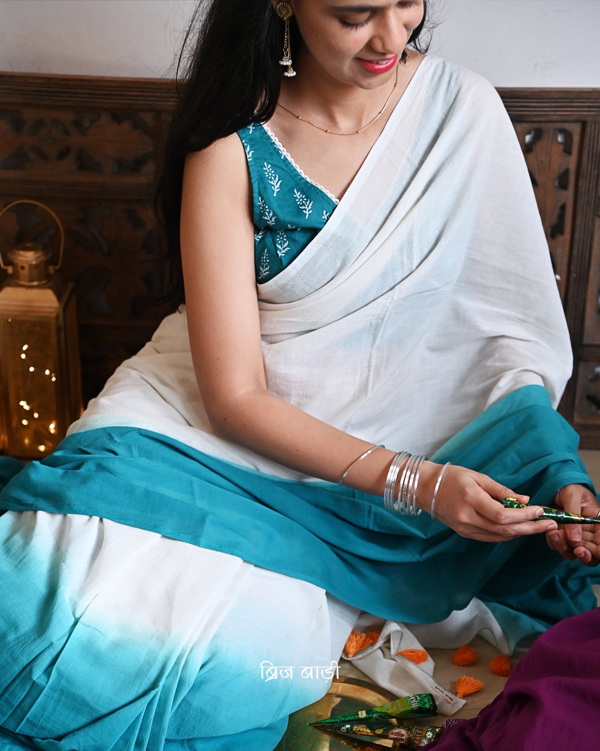 Teal Blue and off-white ombré soft cotton saree by Brij Bari, crafted for effortless elegance and all-day comfort. The subtle blend of tones adds fluidity and grace to the drape, making it perfect for both everyday wear and special occasions. The pallu is adorned with handcrafted orange thread tassels, lending a warm, artisanal touch. It comes with a free hand block printed blouse piece that complements the saree’s minimal yet striking aesthetic. Available in 8 beautiful colour options