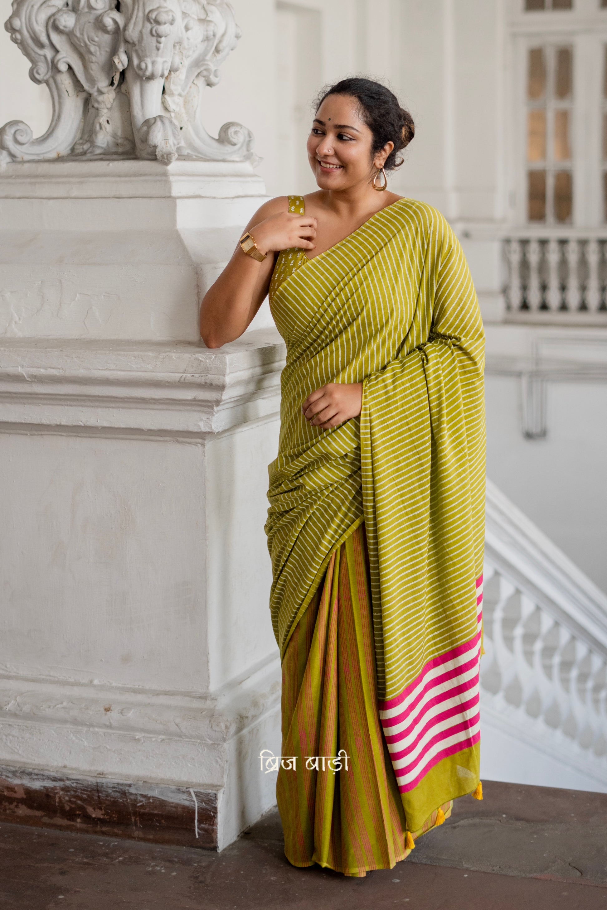 Light green soft and lightweight cotton saree by Brij Bari, hand block printed with pink and white stripe pattern. Finished with handmade yellow thread tassels on the pallu. Includes a free block printed cotton blouse piece. A versatile saree designed to add a vibrant pop of colour to your everyday wardrobe while ensuring breathable comfort and effortless style. Free shipping pan India.