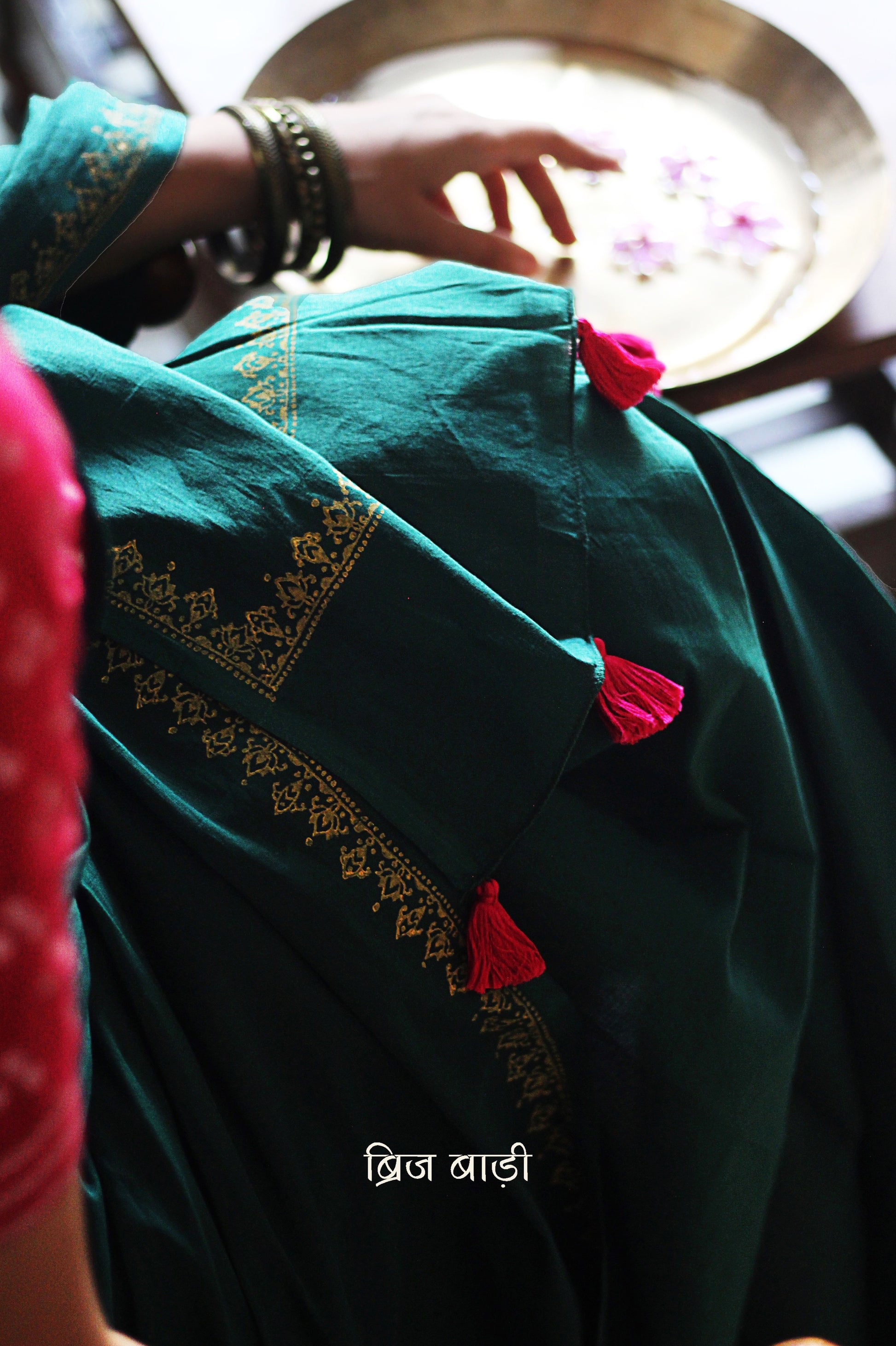 Deep green soft and light-weight cotton saree by Brij Bari, featuring a delicate hand block printed border in vibrant ochre yellow that contrasts beautifully with the rich green. The saree is finished with pink handmade thread tassels on the pallu, adding a touch of traditional charm. It comes with a free matching block printed blouse piece, completing the handcrafted look. Perfect for everyday wear, casual outings, or semi-formal occasions, with free shipping pan India.
