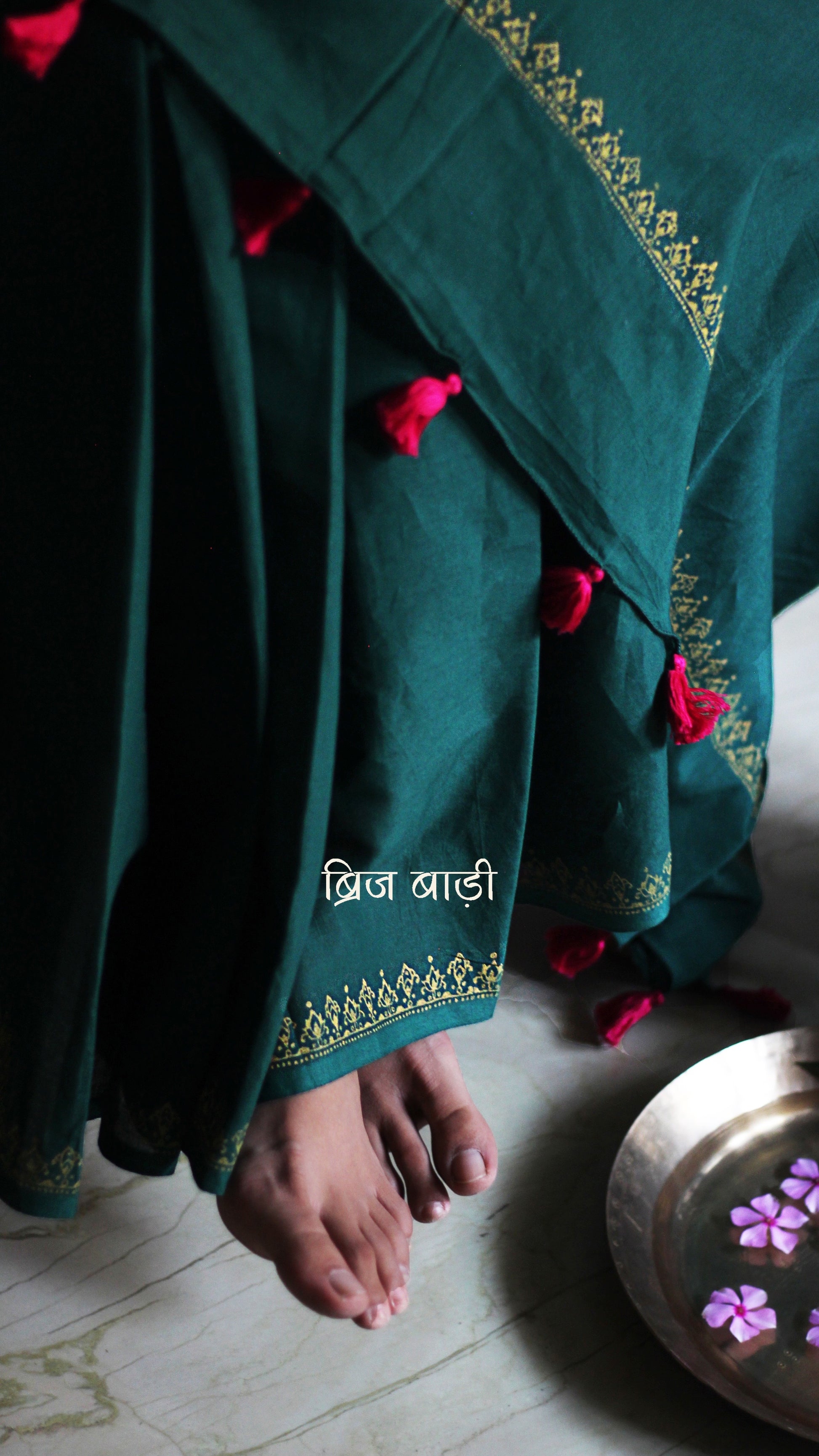 Deep green soft and light-weight cotton saree by Brij Bari, featuring a delicate hand block printed border in vibrant ochre yellow that contrasts beautifully with the rich green. The saree is finished with pink handmade thread tassels on the pallu, adding a touch of traditional charm. It comes with a free matching block printed blouse piece, completing the handcrafted look. Perfect for everyday wear, casual outings, or semi-formal occasions, with free shipping pan India.