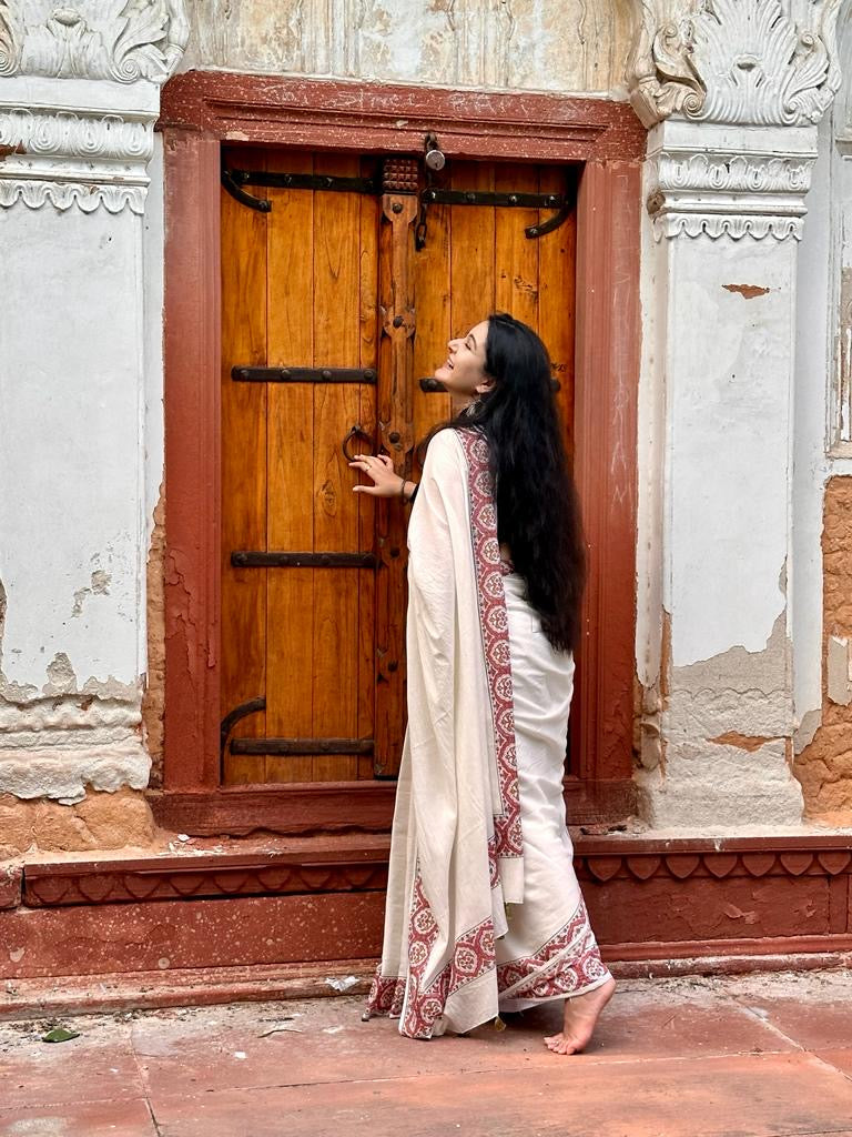 Sonal Singh a senior textile designer wearing our Parthivi saree. Off white soft and light-weight cotton saree by Brij Bari, featuring a delicate and intricate multicolour hand block printed border crafted by skilled artisans. Designed for all-day comfort and effortless style, this saree is detailed with olive green handmade thread tassels on the pallu. It comes with a free block printed blouse piece, making it a versatile pick for everyday wear, casual gatherings, and relaxed festive occasions. 