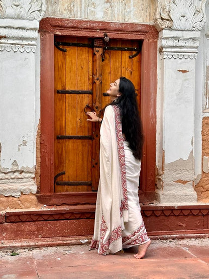 Sonal Singh a senior textile designer wearing our Parthivi saree. Off white soft and light-weight cotton saree by Brij Bari, featuring a delicate and intricate multicolour hand block printed border crafted by skilled artisans. Designed for all-day comfort and effortless style, this saree is detailed with olive green handmade thread tassels on the pallu. It comes with a free block printed blouse piece, making it a versatile pick for everyday wear, casual gatherings, and relaxed festive occasions. 