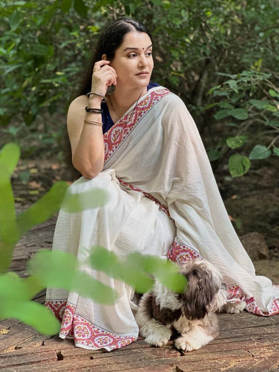 Sonal Singh a senior textile designer wearing our Parthivi saree. Off white soft and light-weight cotton saree by Brij Bari, featuring a delicate and intricate multicolour hand block printed border crafted by skilled artisans. Designed for all-day comfort and effortless style, this saree is detailed with olive green handmade thread tassels on the pallu. It comes with a free block printed blouse piece, making it a versatile pick for everyday wear, casual gatherings, and relaxed festive occasions. 