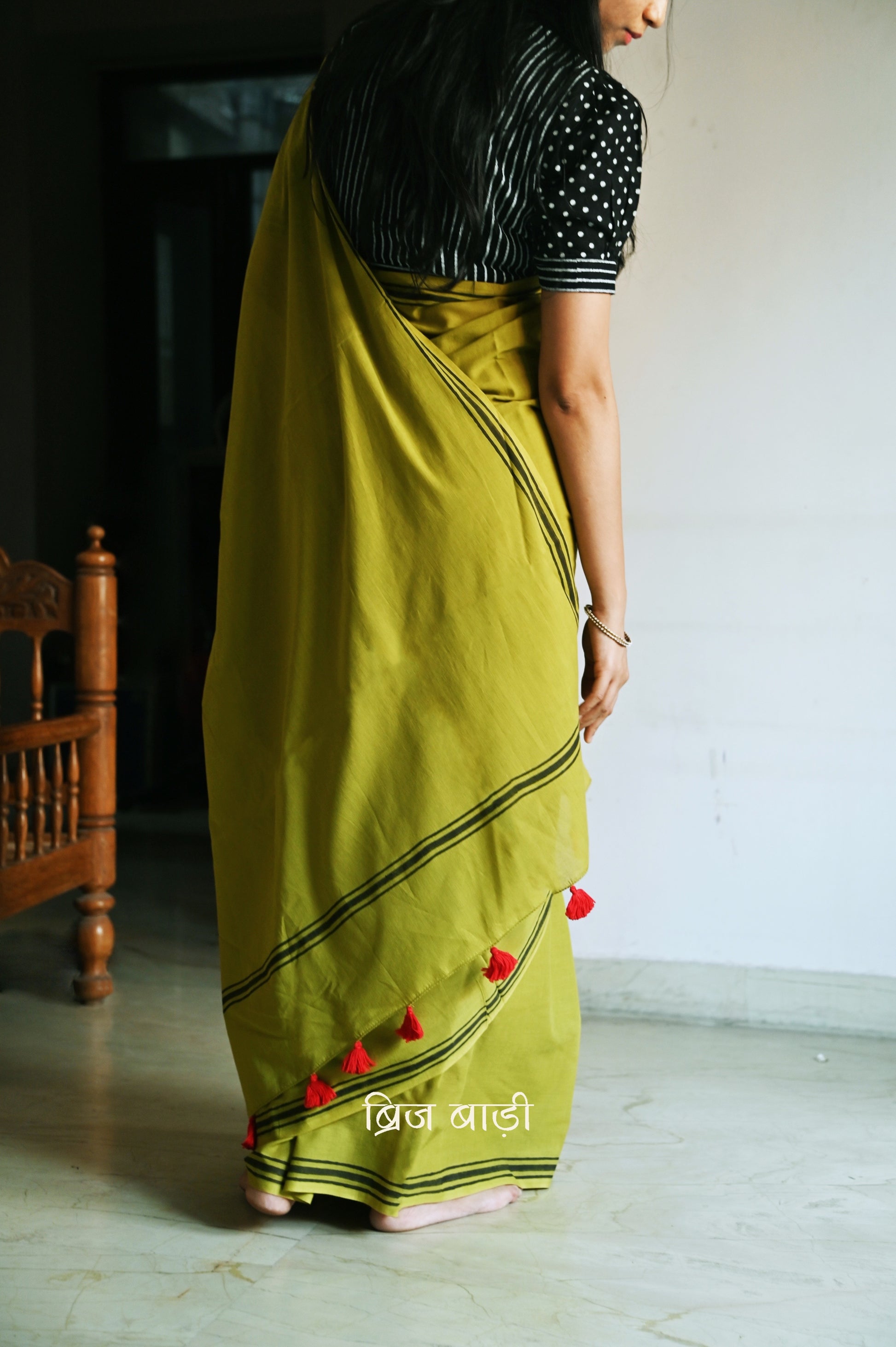 Light green soft and light-weight cotton saree by Brij Bari, crafted with a simple yet elegant black hand block printed stripe border. The saree is adorned with red handmade thread tassels on the pallu, adding a vibrant touch. It comes with a free matching block printed blouse piece, offering a complete handcrafted look. Available in 2 colours, designed for all-day comfort and style, perfect for casual and everyday wear. Free shipping available pan India.